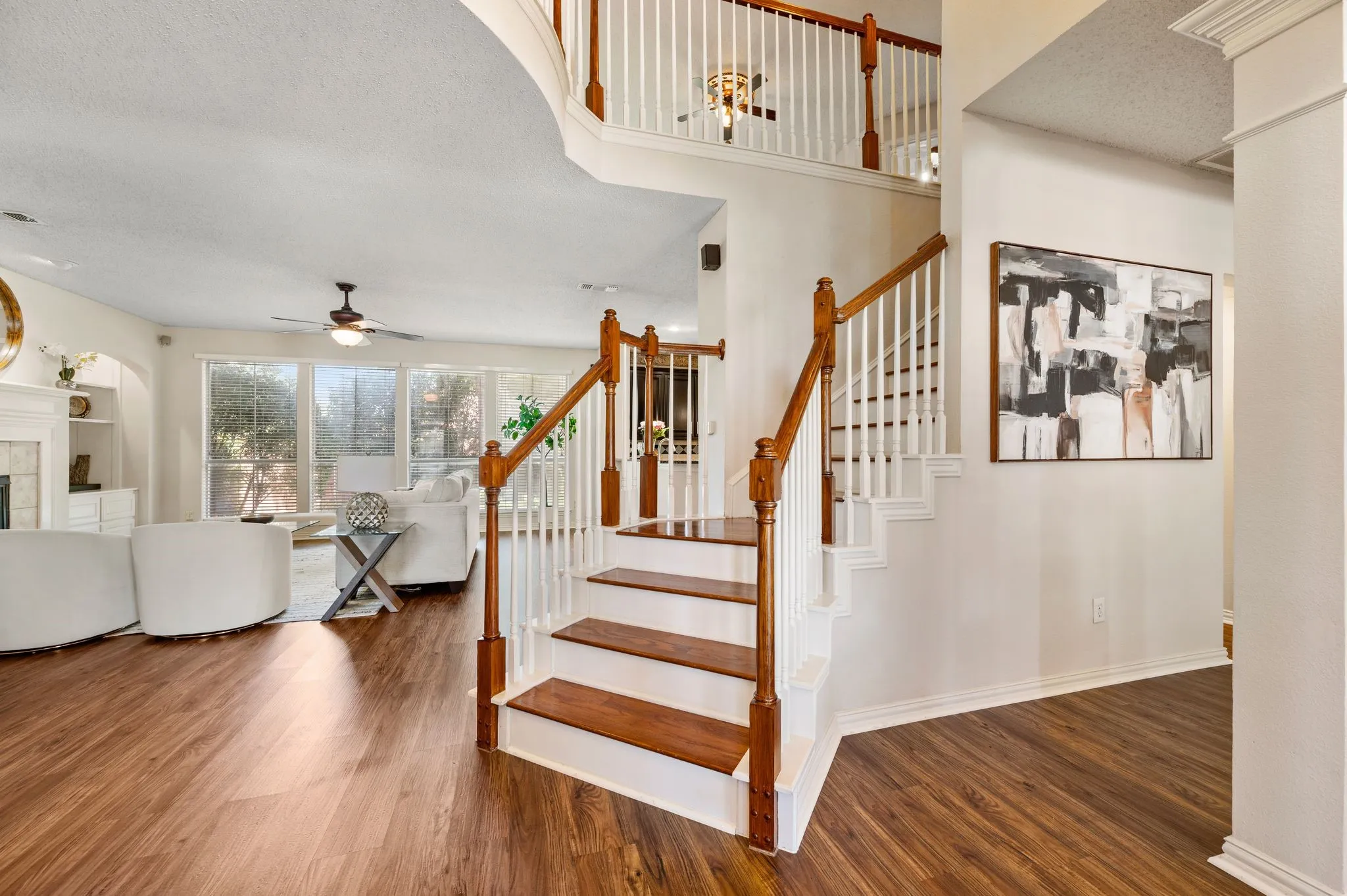 Wood-finish flooring throughout, bright living area with large windows, staircase with wood handrails and white balusters, and a multi-level ceiling