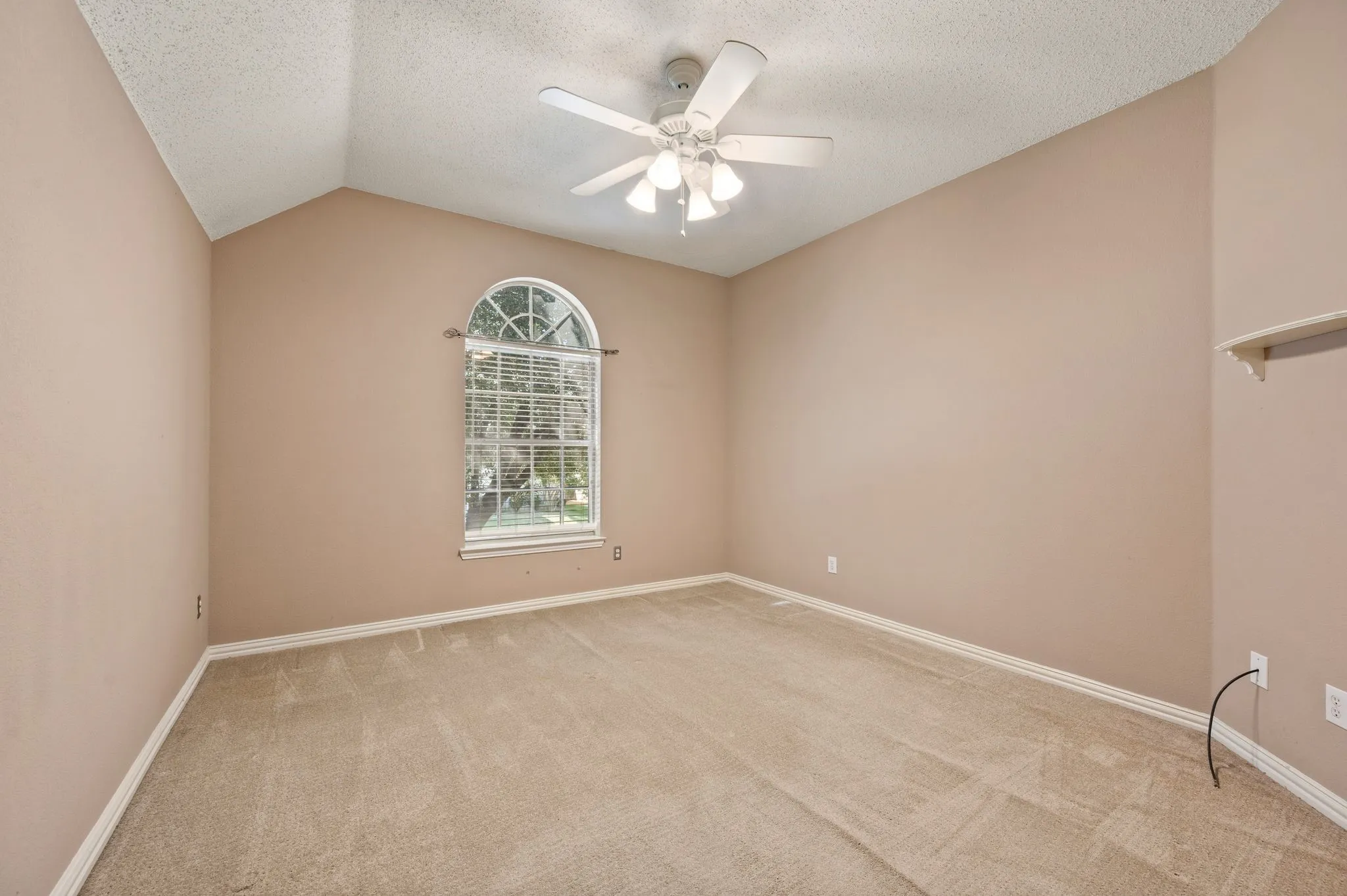 Vaulted ceiling, arched window, ceiling fan, neutral wall tones, and carpeted flooring
