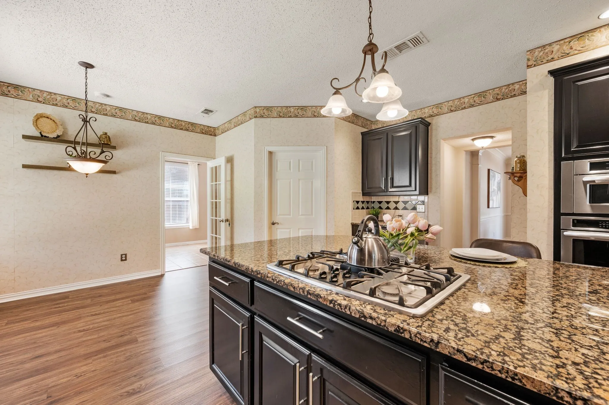 Kitchen island with a built-in gas range, granite countertop, dark wood-finish cabinetry, and stainless steel appliances