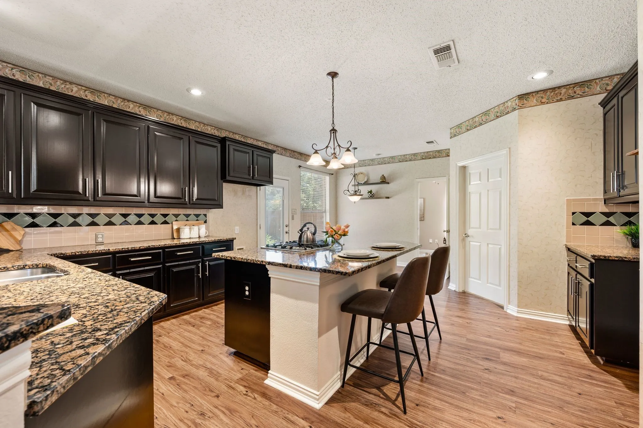 Kitchen featuring wood-finish flooring, dark wood cabinetry, granite countertops, and a tile backsplash