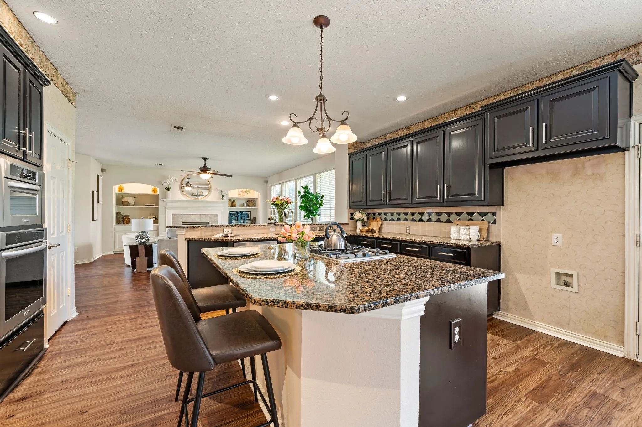 Open-concept kitchen with wood-finish flooring, granite countertops, dark wood cabinetry, and stainless steel built-in appliances