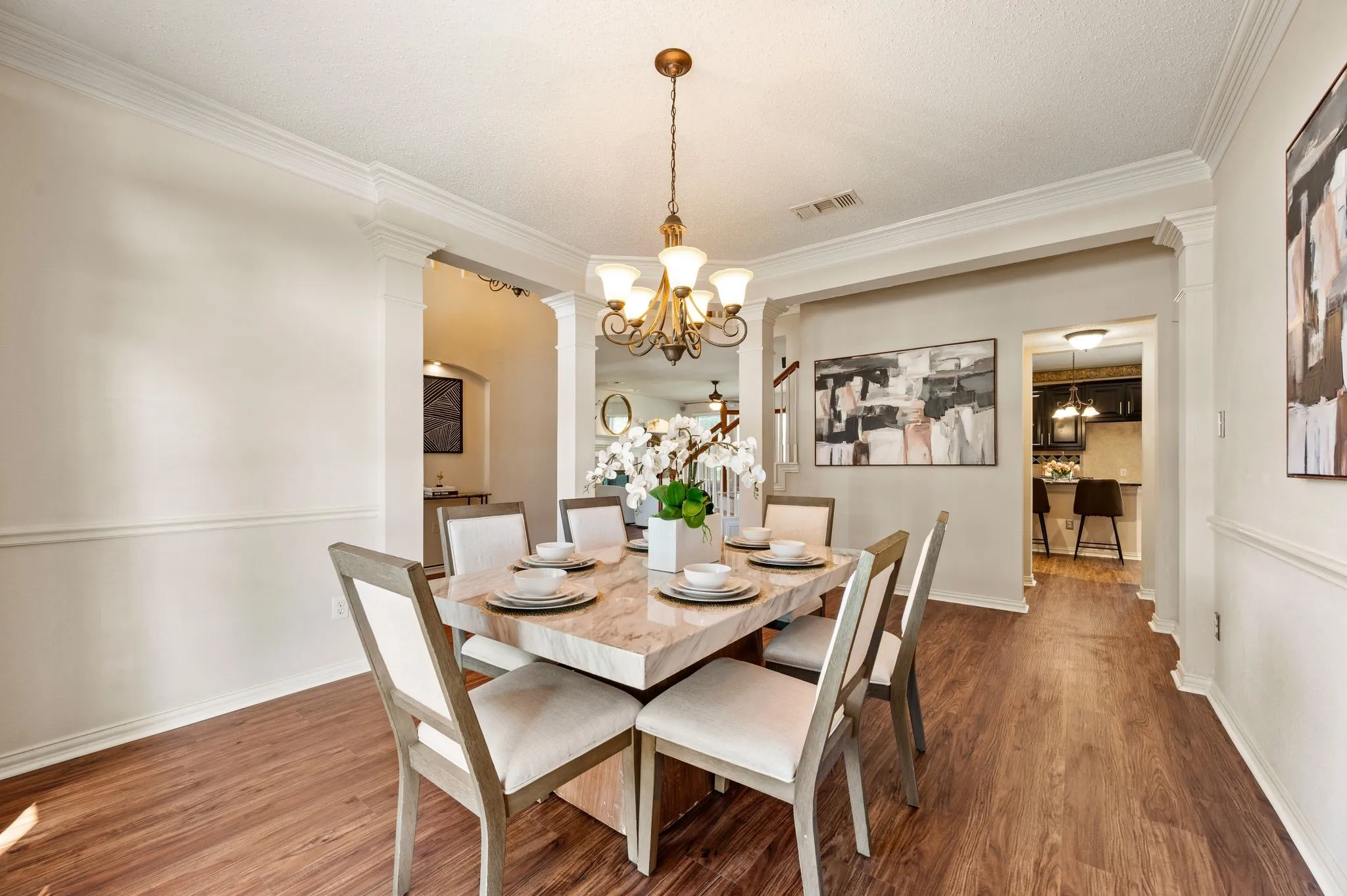 Wood-finish flooring throughout, crown molding, chair rail molding, decorative columns, and a chandelier with glass shades