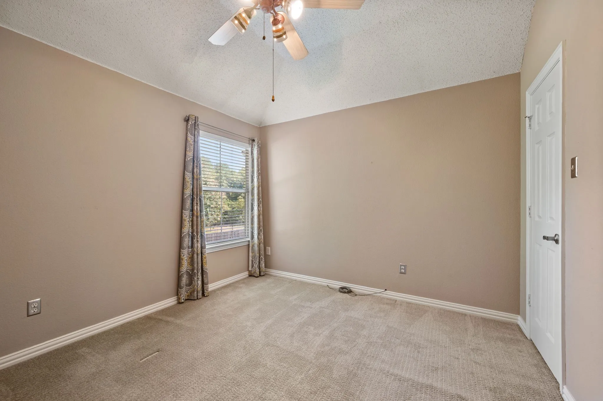 Carpeted room featuring a ceiling fan with integrated lighting, a window with blinds, and a white paneled door
