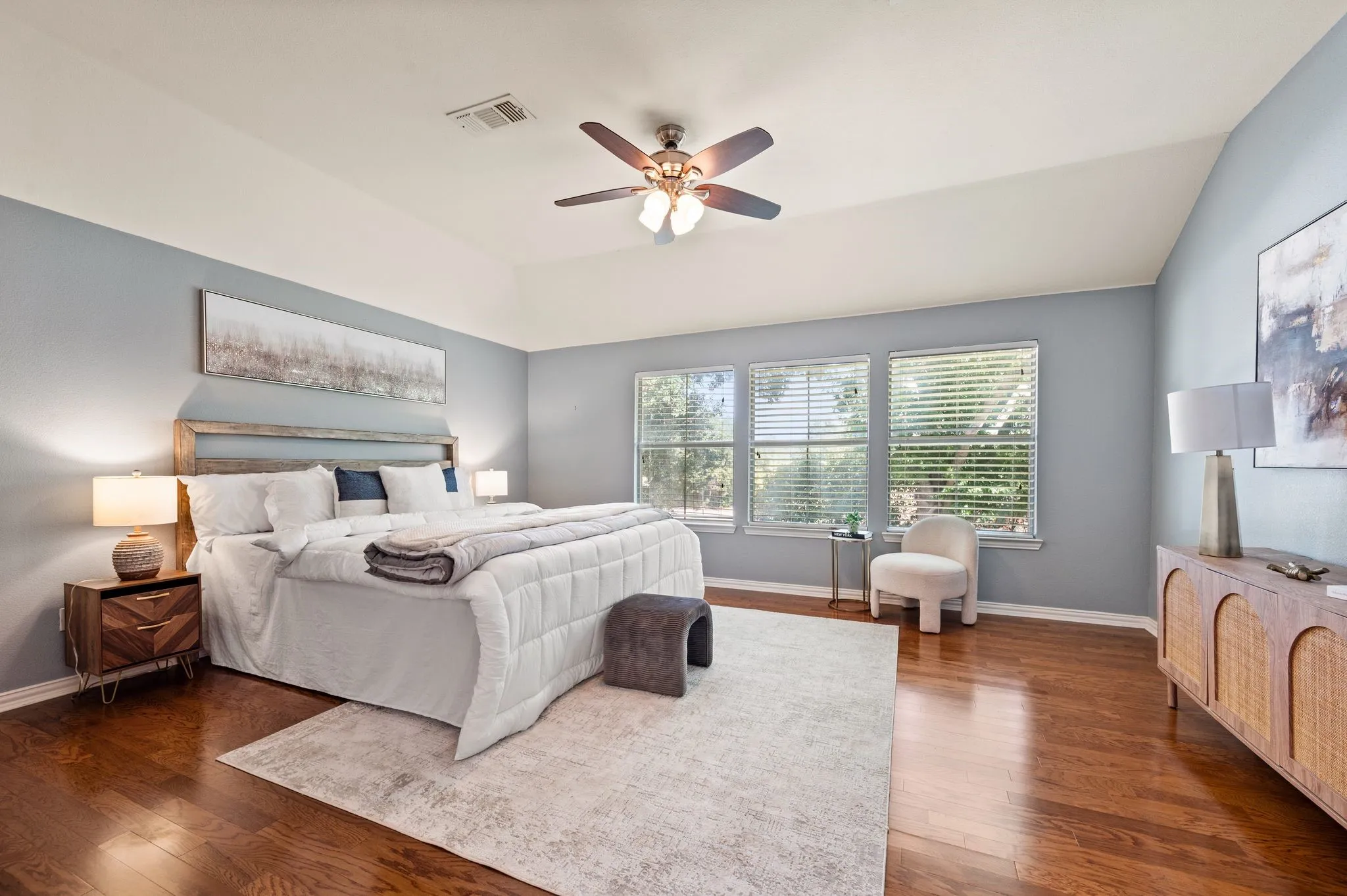 Vaulted ceiling with a ceiling fan, three windows with blinds, and wood-finish flooring