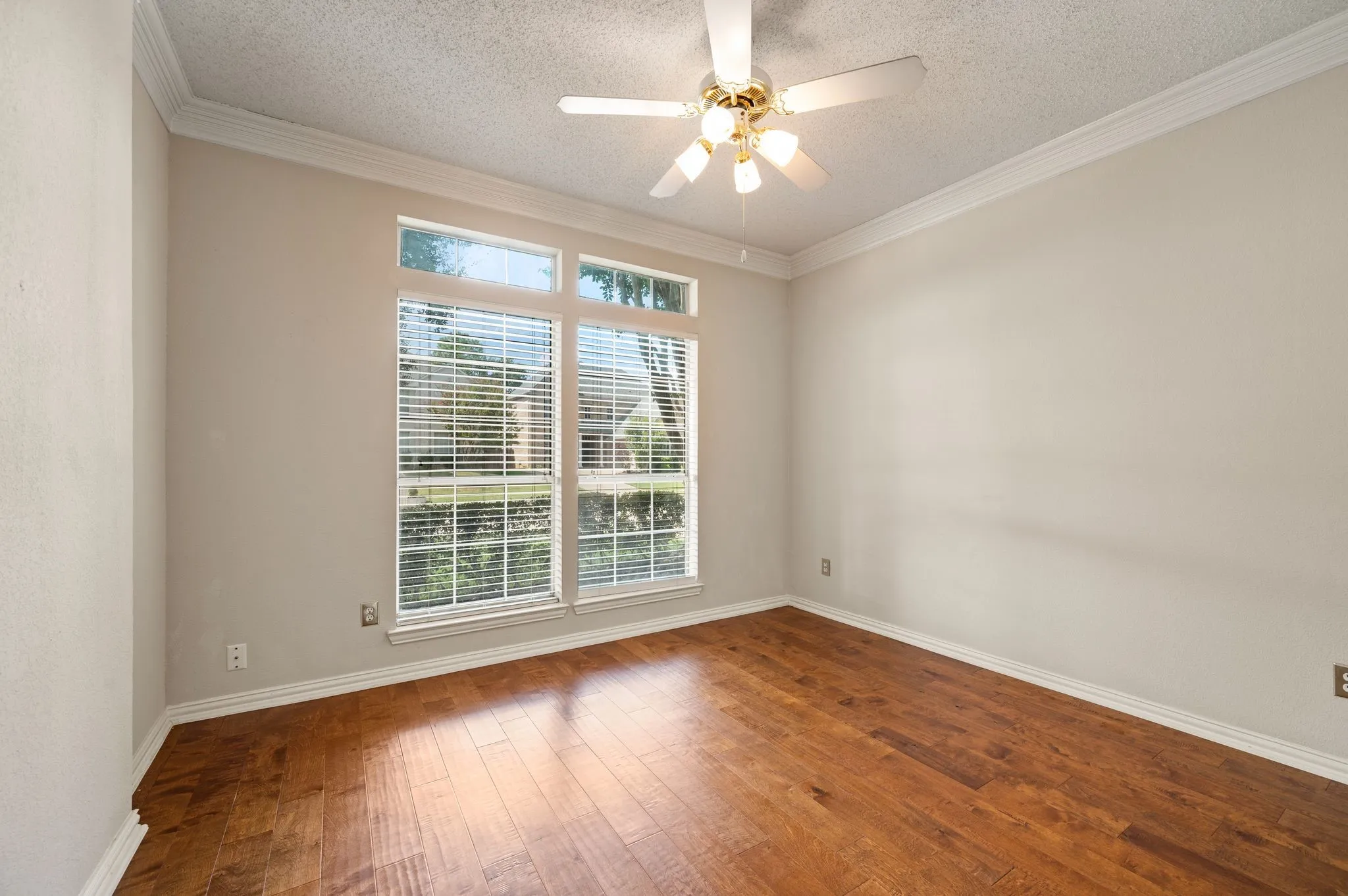 Hardwood flooring, crown molding, a ceiling fan with integrated lighting, and a large multi-pane window