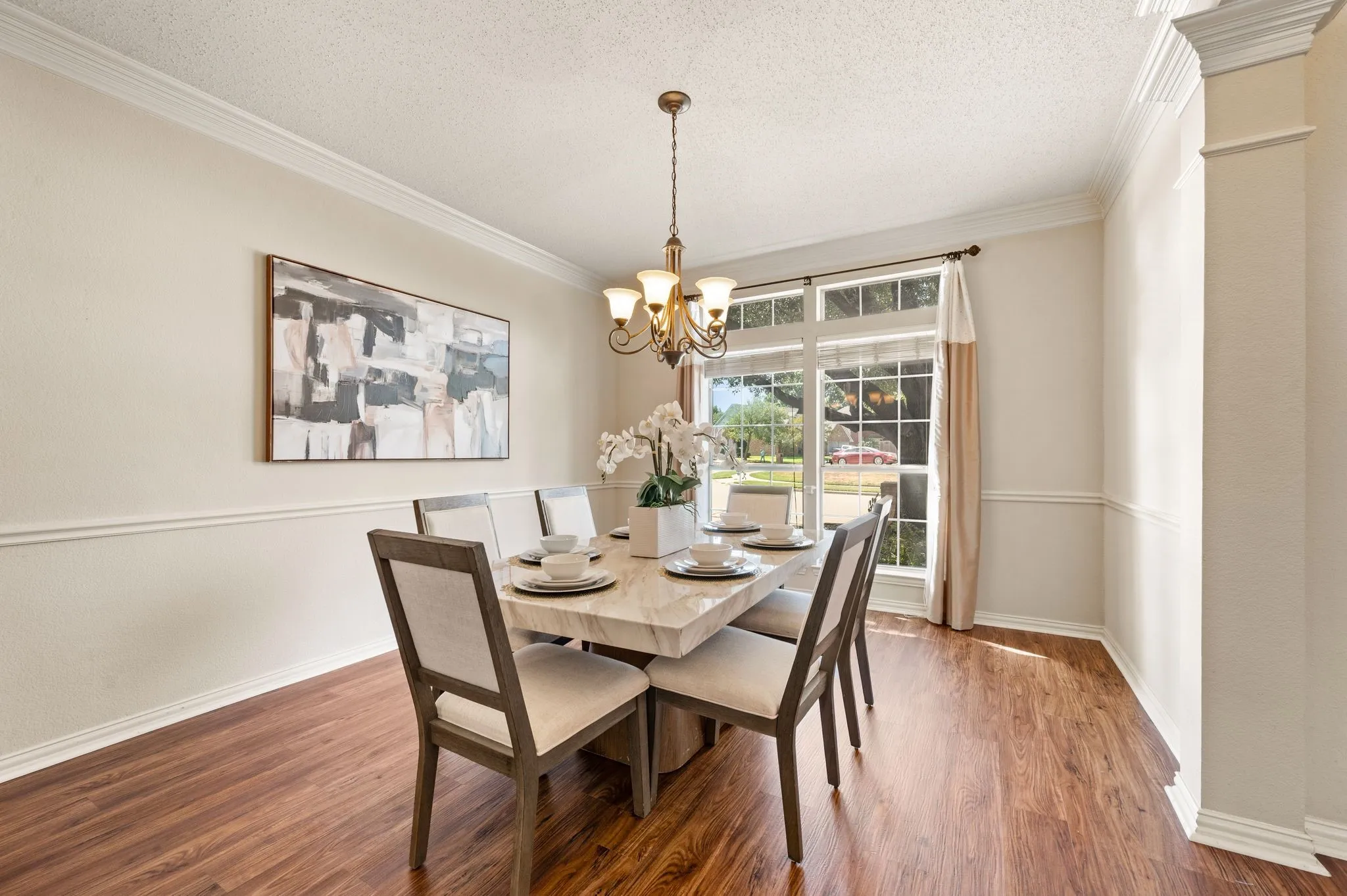 Wood-finish flooring, decorative wall molding, large window with muntins, and a multi-arm chandelier