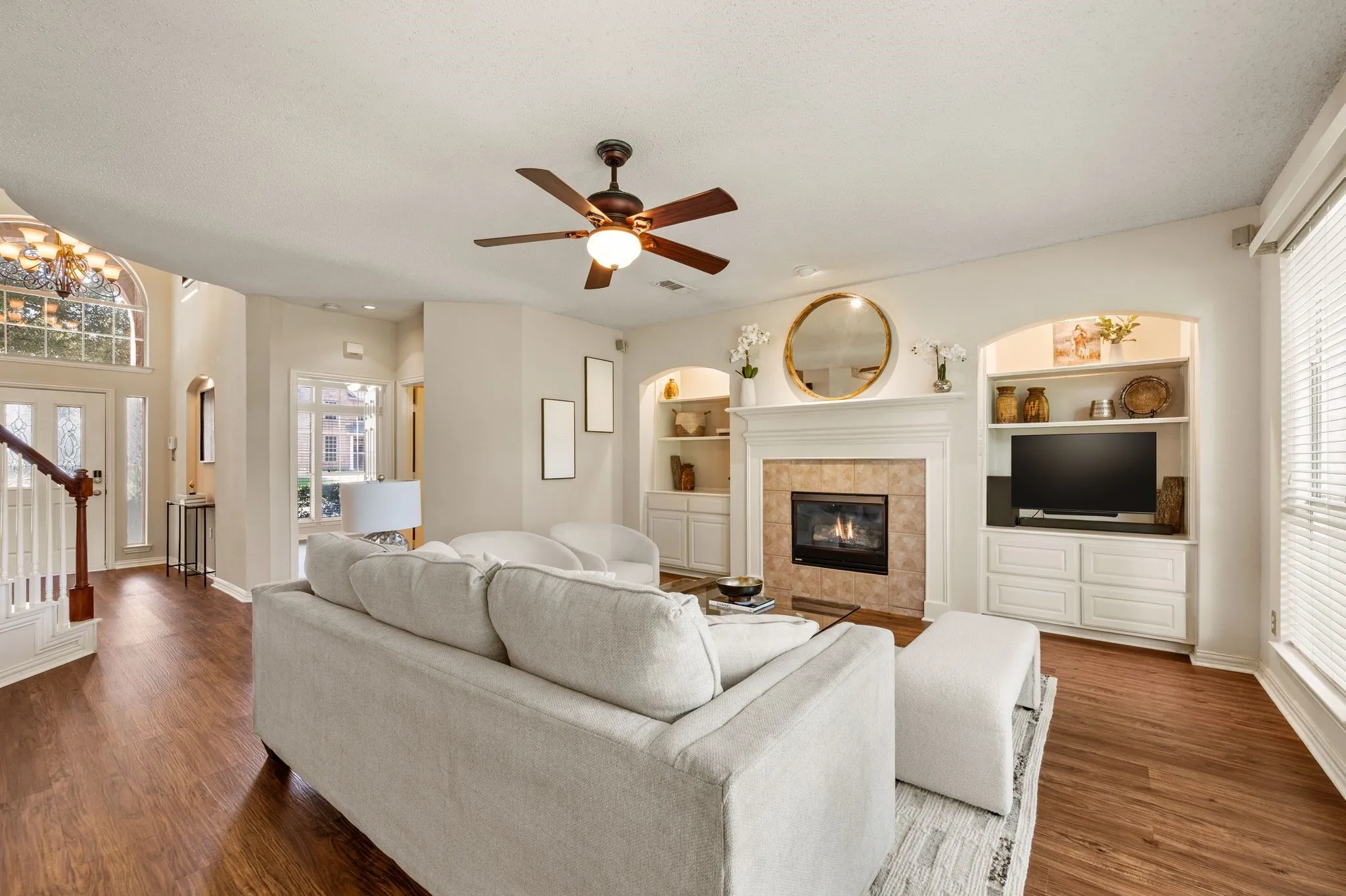 Living area with wood-finish flooring, a ceiling fan, and a fireplace featuring a tile surround and mantel
