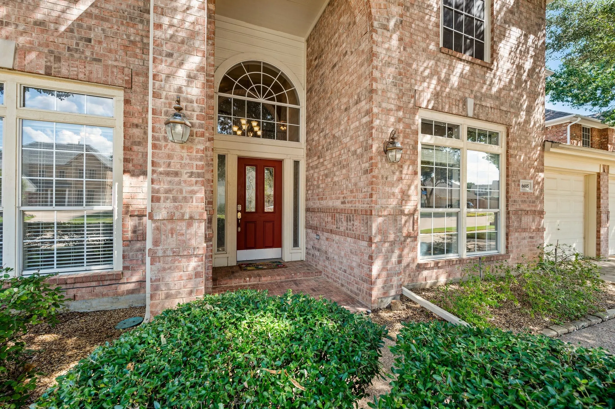 Brick exterior with white-framed windows, a red front door, and an arched transom window above the entrance