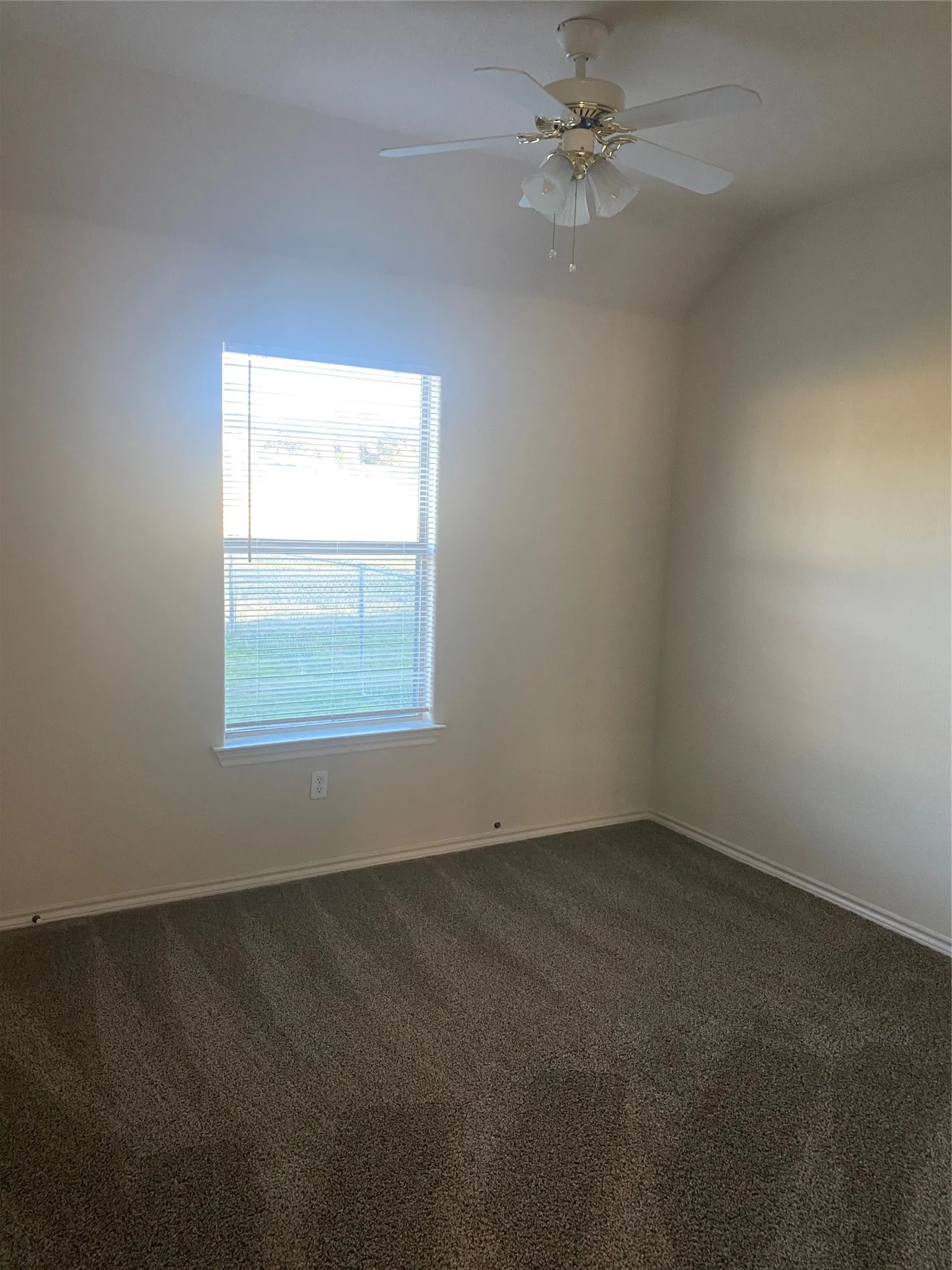 Neutral-toned walls, vaulted ceiling, ceiling fan with integrated lighting, window with horizontal blinds, and carpeting
