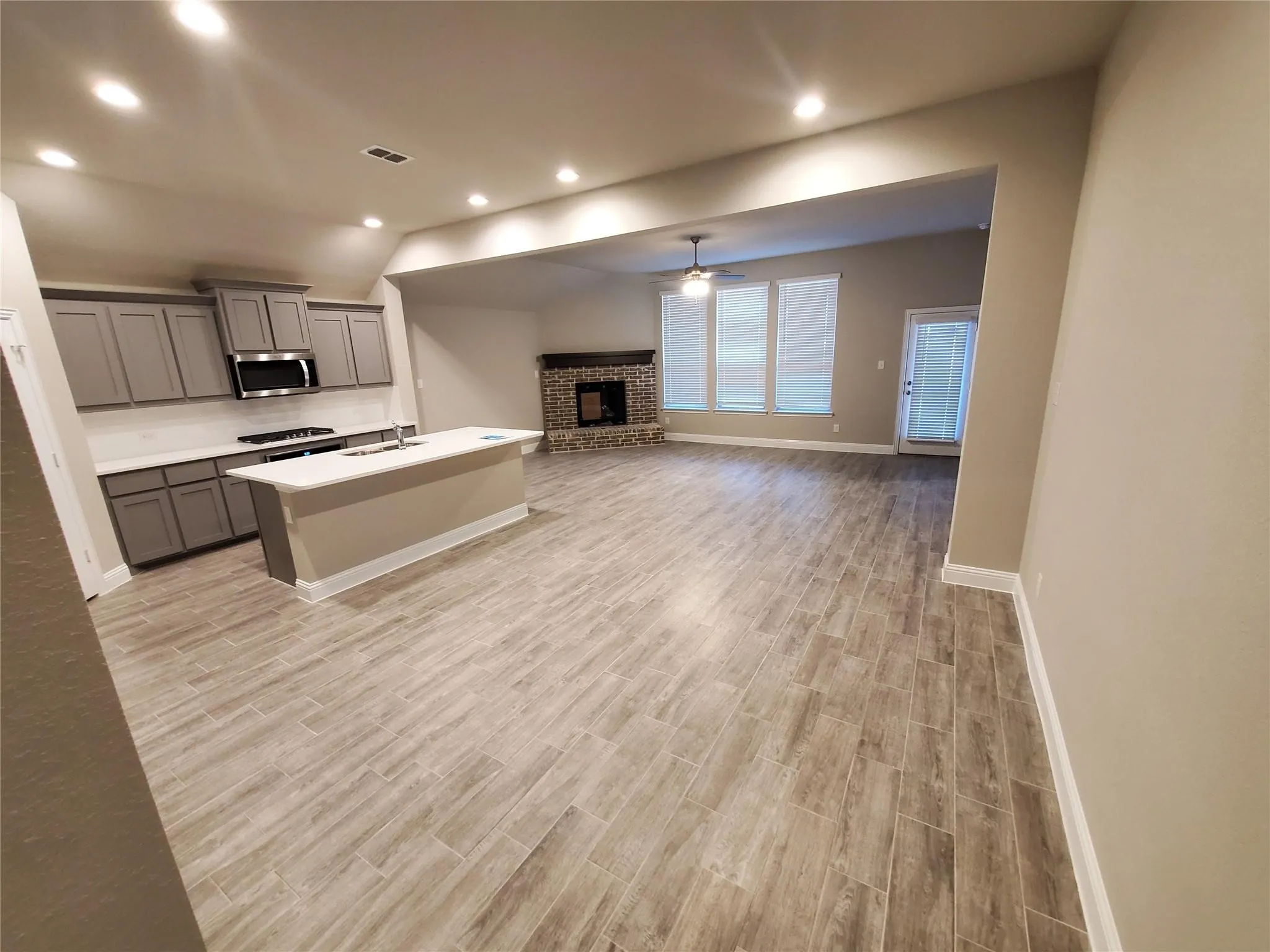 Open-concept layout with wood-finish tile flooring, a kitchen island with sink, gray cabinetry, and a stone fireplace