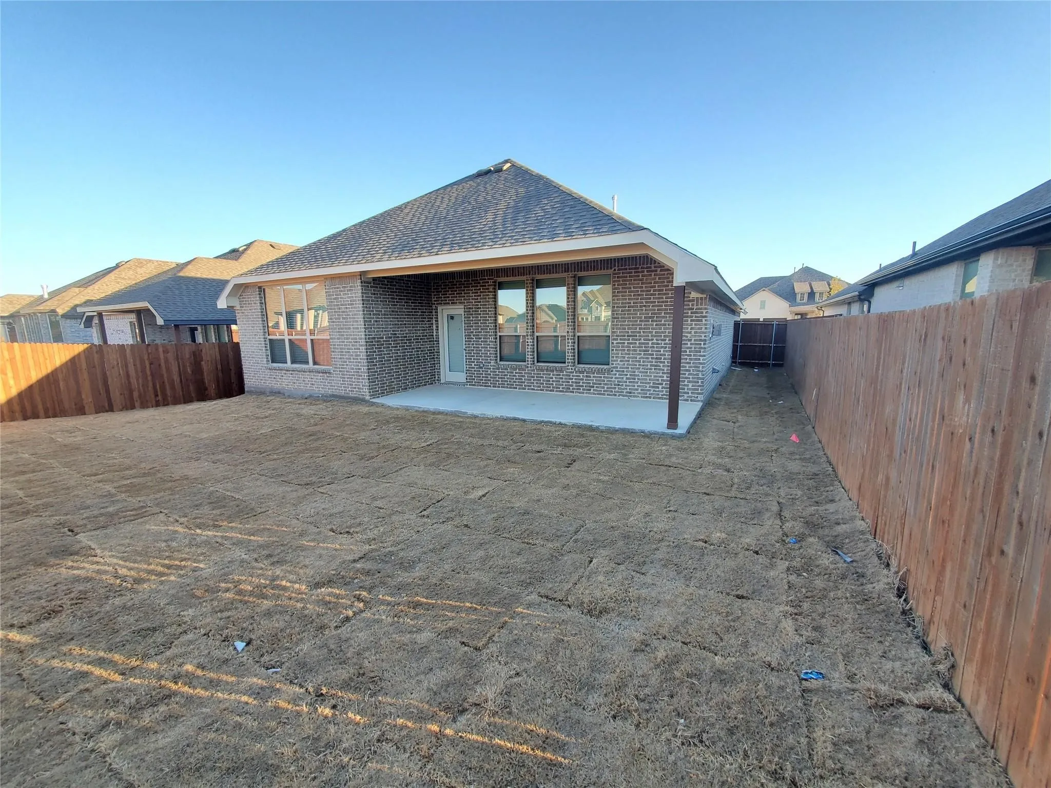 Brick exterior with an expansive backyard featuring a covered patio, wood fencing, and a concrete slab