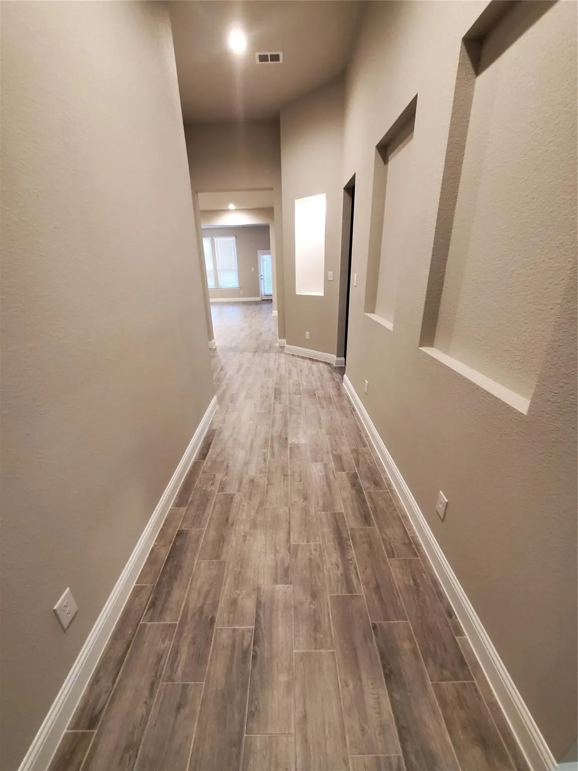 Hallway with wood-look tile flooring, neutral wall tones, decorative wall niches, and recessed lighting