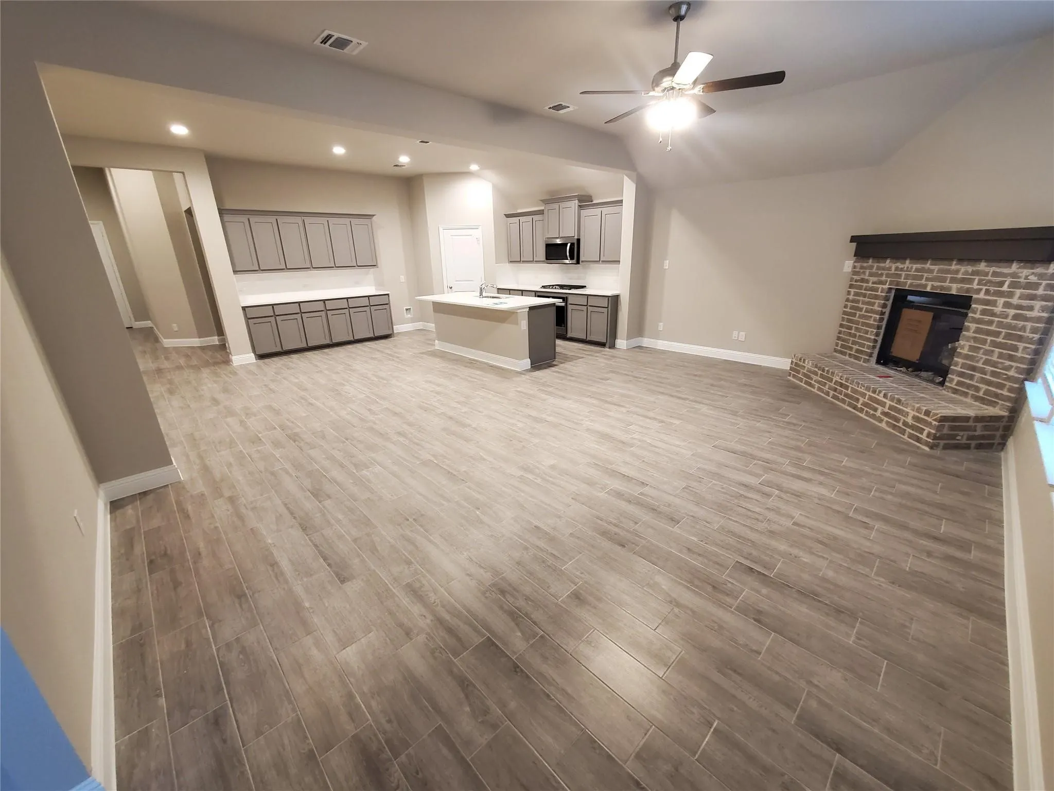 Spacious living area featuring wood-finish tile flooring, recessed lighting, and a prominent brick fireplace