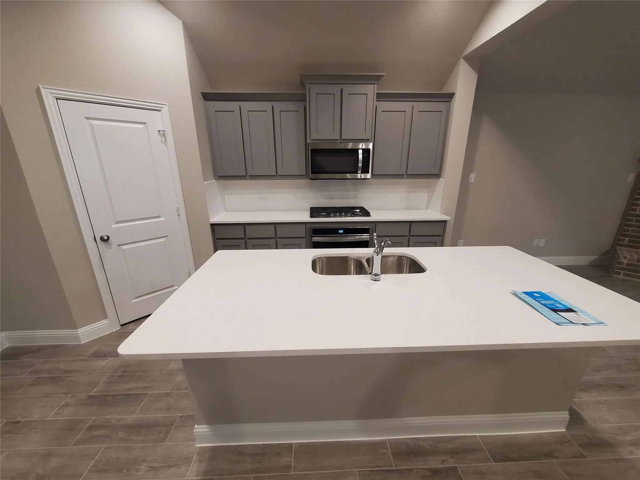 Spacious kitchen island with a double basin sink, stainless steel appliances, grey cabinetry, and tile flooring