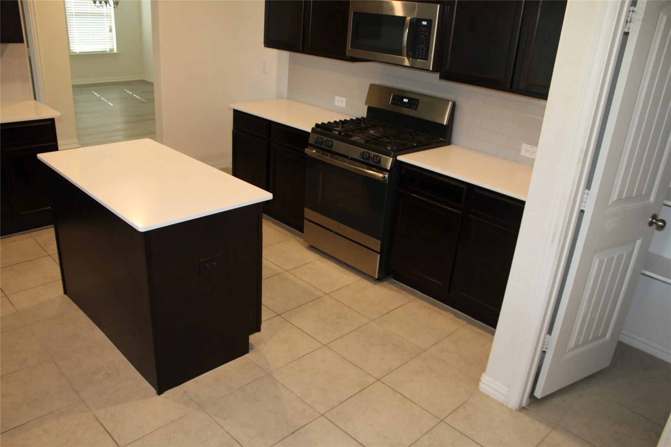 Kitchen featuring a central island, dark wood-finish cabinetry, light-toned countertops, and stainless steel appliances