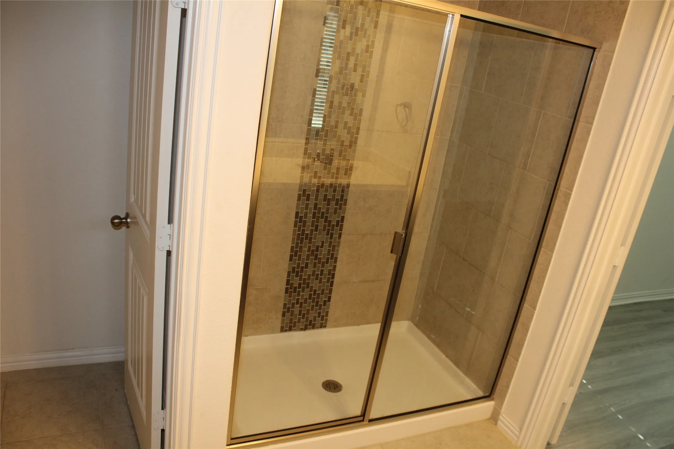 Shower enclosure with sliding glass doors, tiled walls, decorative mosaic tile accent, and a white shower pan