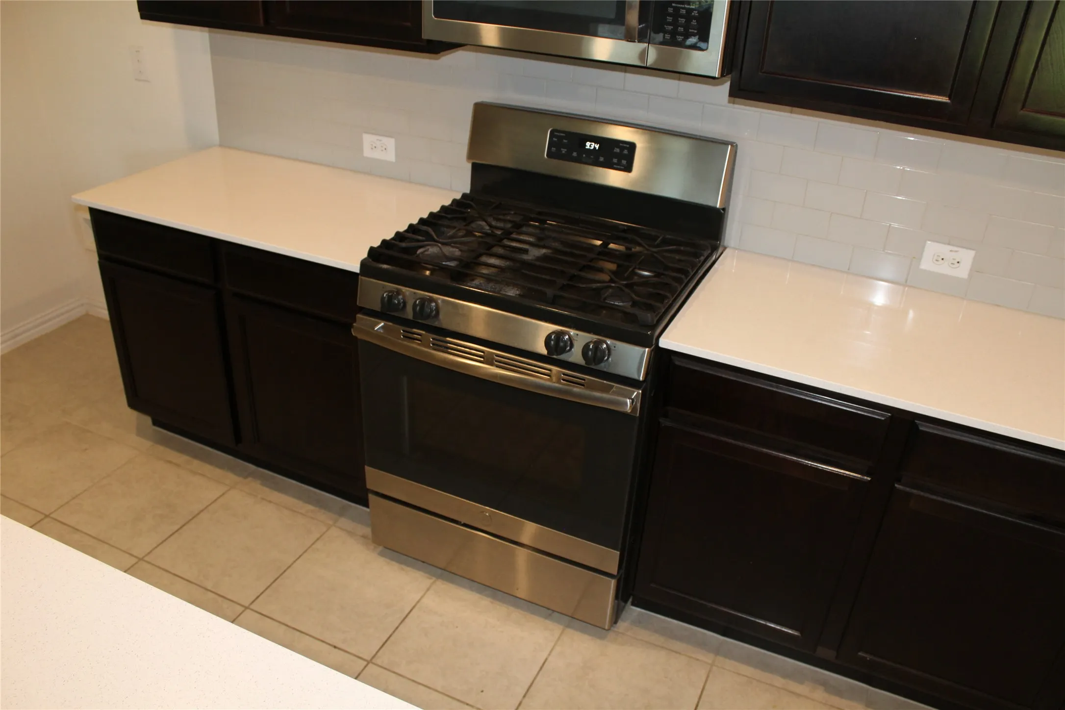 Stainless steel gas range, white countertops, dark wood-finish cabinetry, subway tile backsplash, and ceramic tile flooring