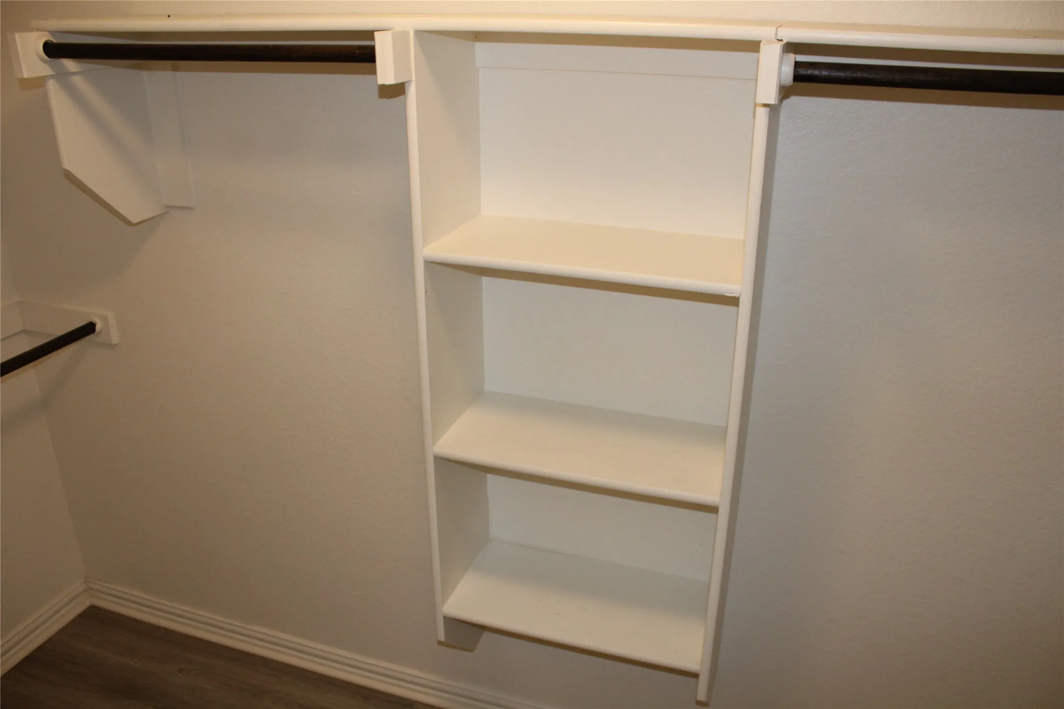 Built-in shelving with three shelves, two clothing rods, and wood-finish flooring