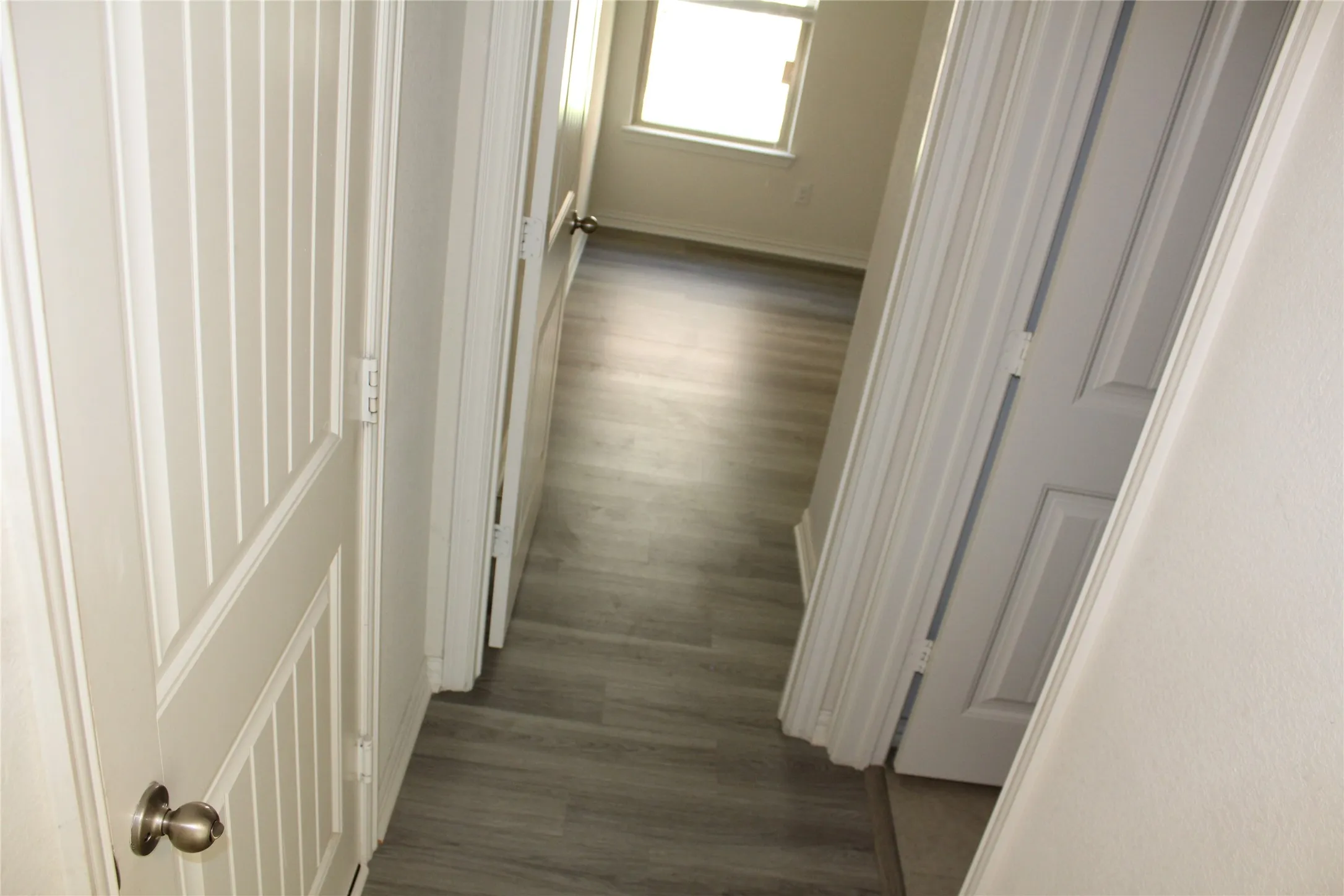 Wood-finish flooring extending into the room, white paneled doors, and natural light from the window