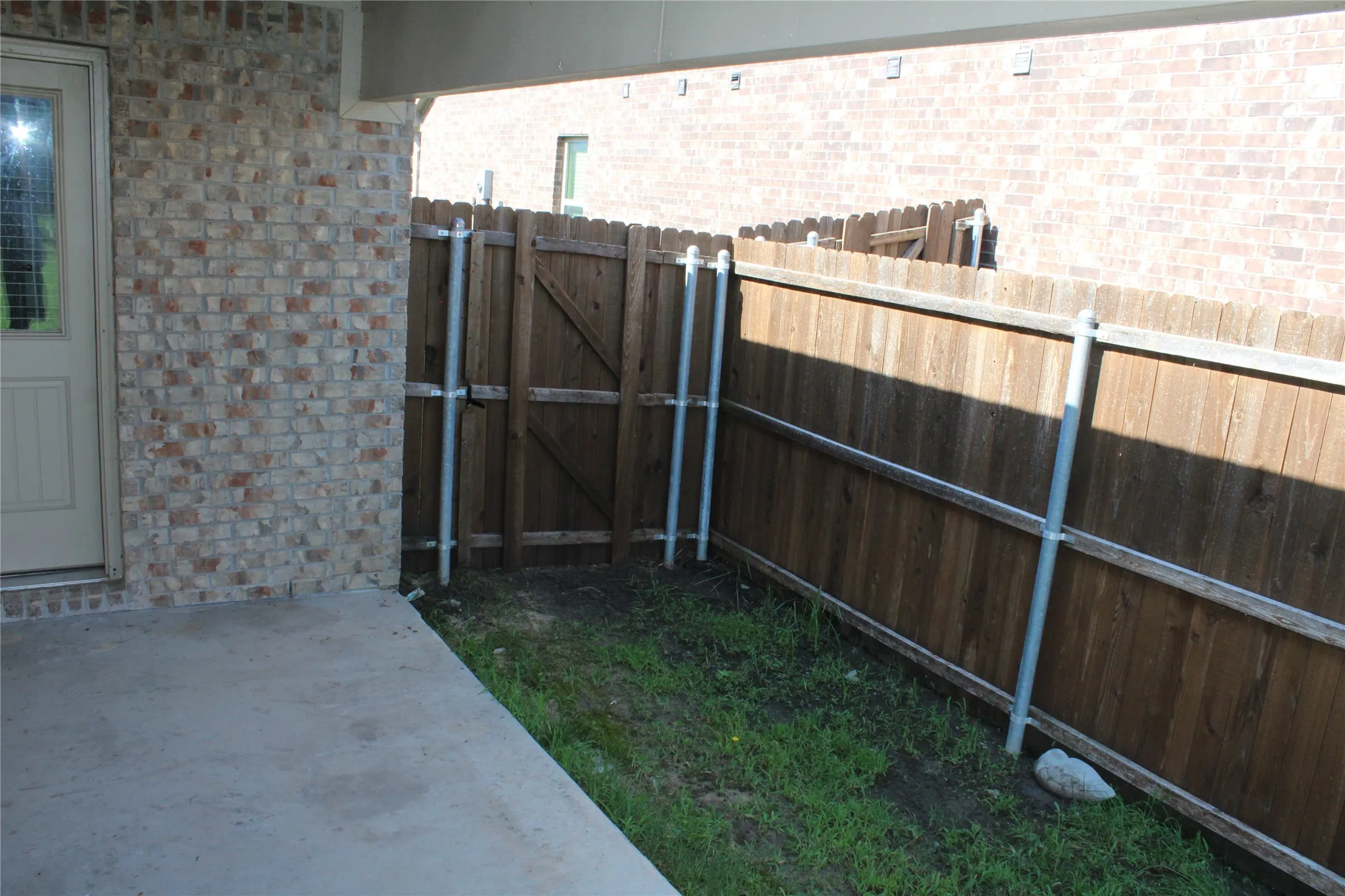 Covered concrete patio with a brick exterior wall and wood privacy fencing