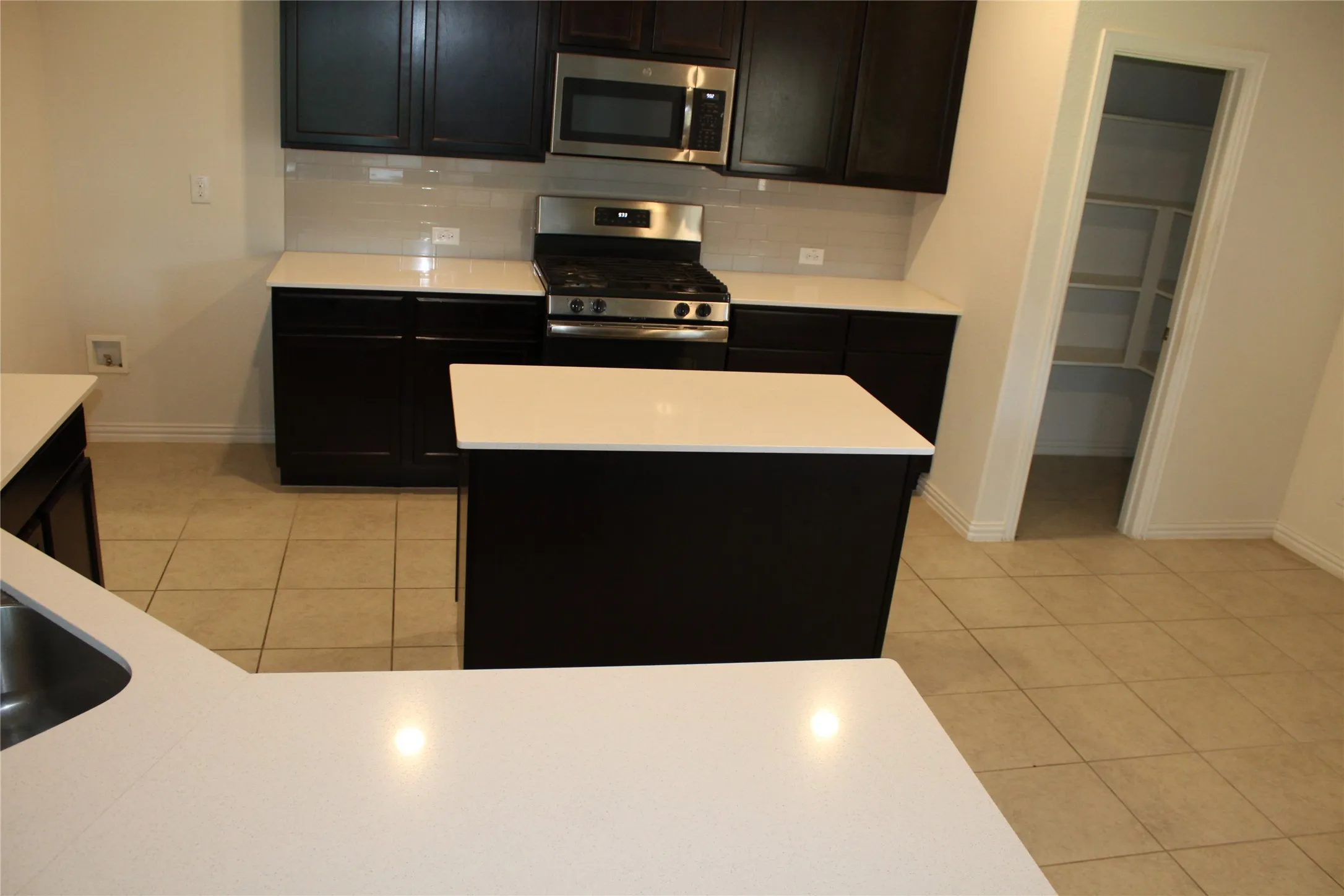 Kitchen featuring dark wood cabinetry, white countertops, tile flooring, stainless steel appliances, and a pantry with shelving