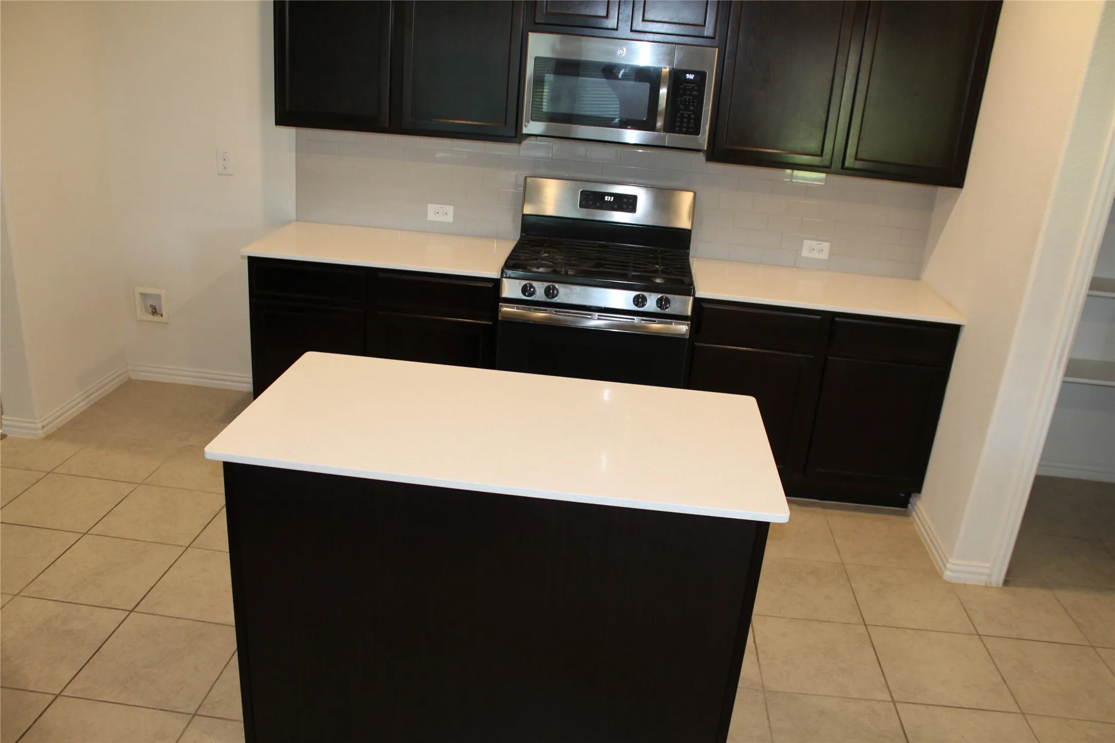 Kitchen featuring dark wood cabinetry, white countertops, tile flooring, stainless steel gas range, and a stainless steel microwave