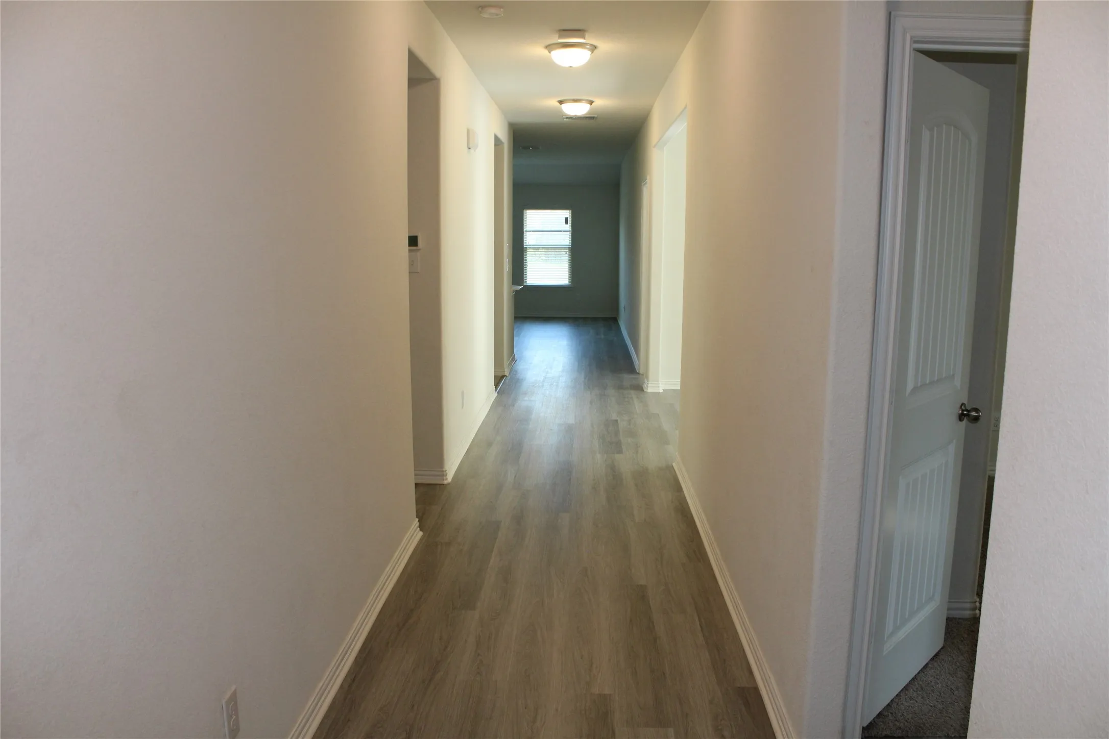 Hallway featuring wood-finish flooring, flush mount lighting, and light-toned walls