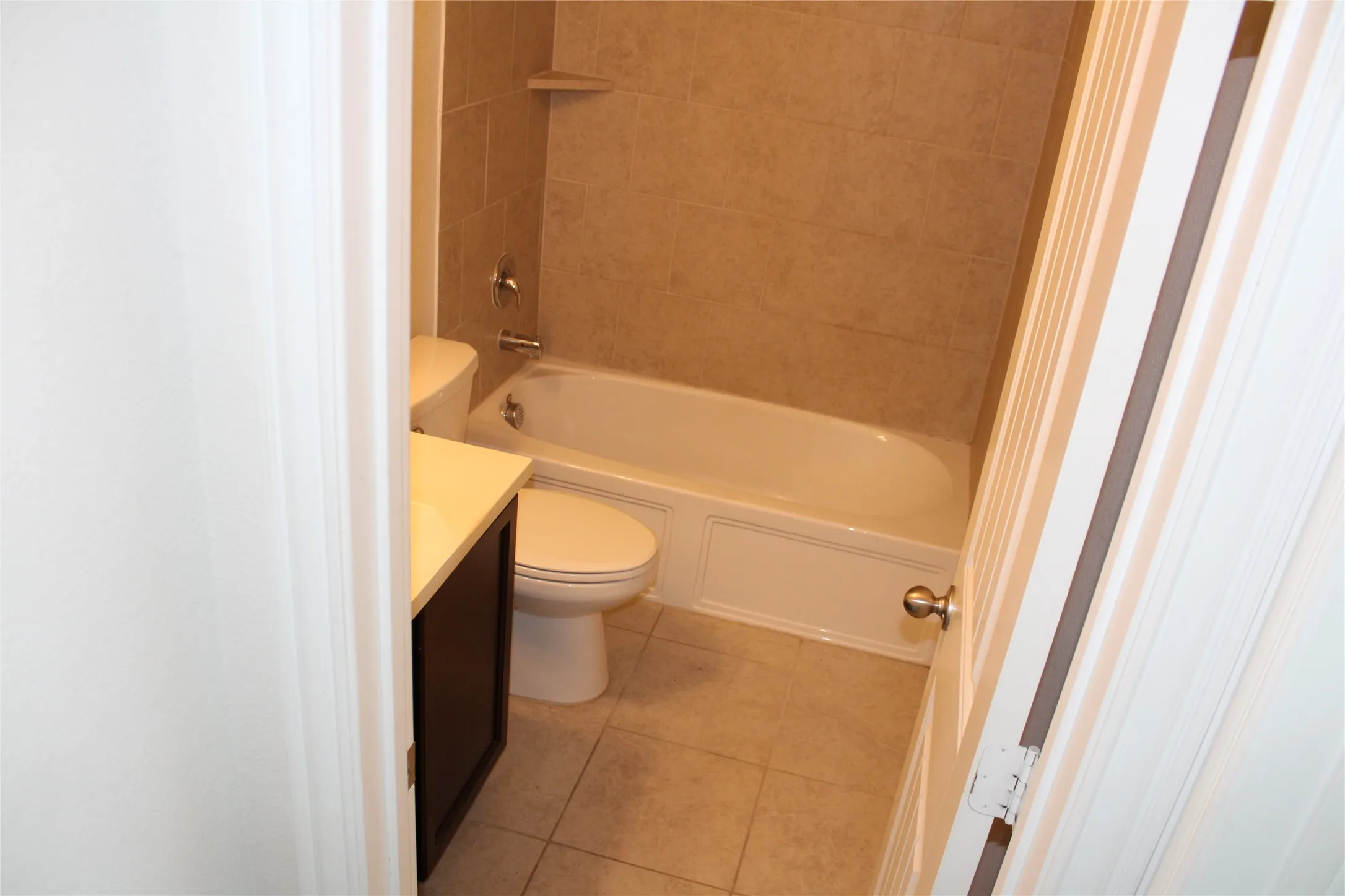 Bathroom featuring a tub/shower combination with tiled surround, a built-in corner shelf, a dark wood-finish vanity, a light-colored countertop, and tiled flooring