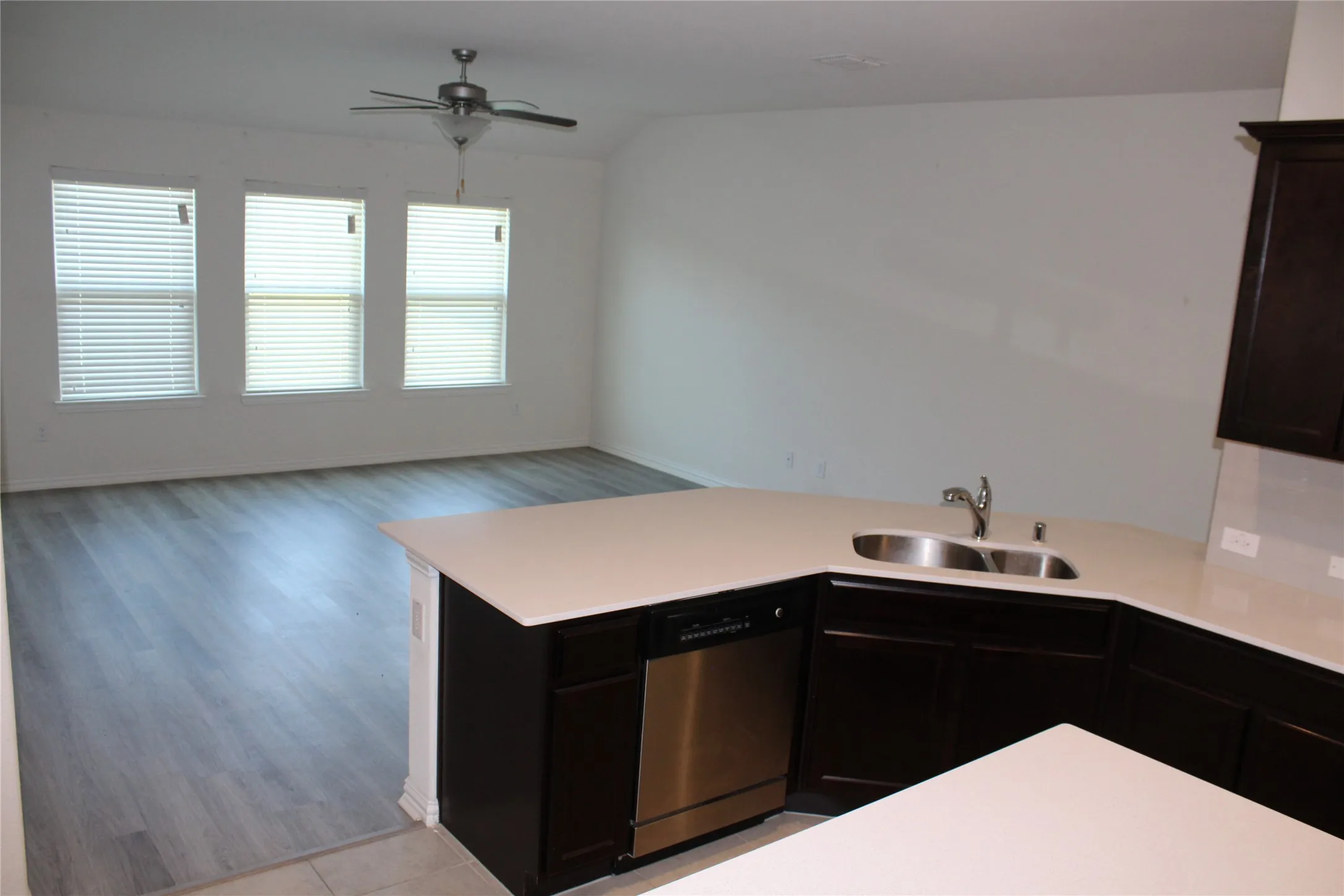 Open-concept living area with wood-finish flooring, three large windows, and a ceiling fan