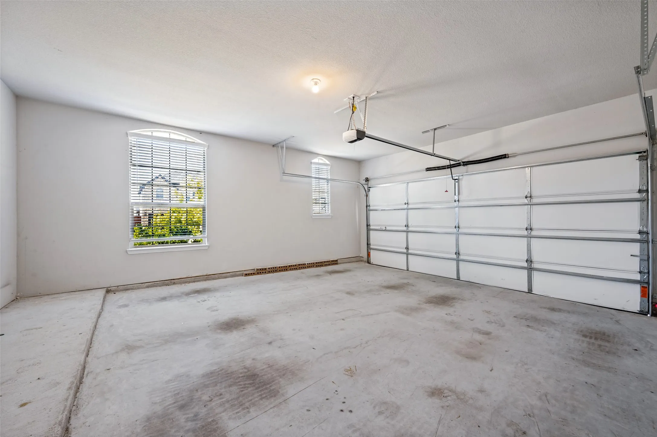 Concrete flooring, automatic garage door opener, two arched windows with blinds, and ceiling-mounted lighting