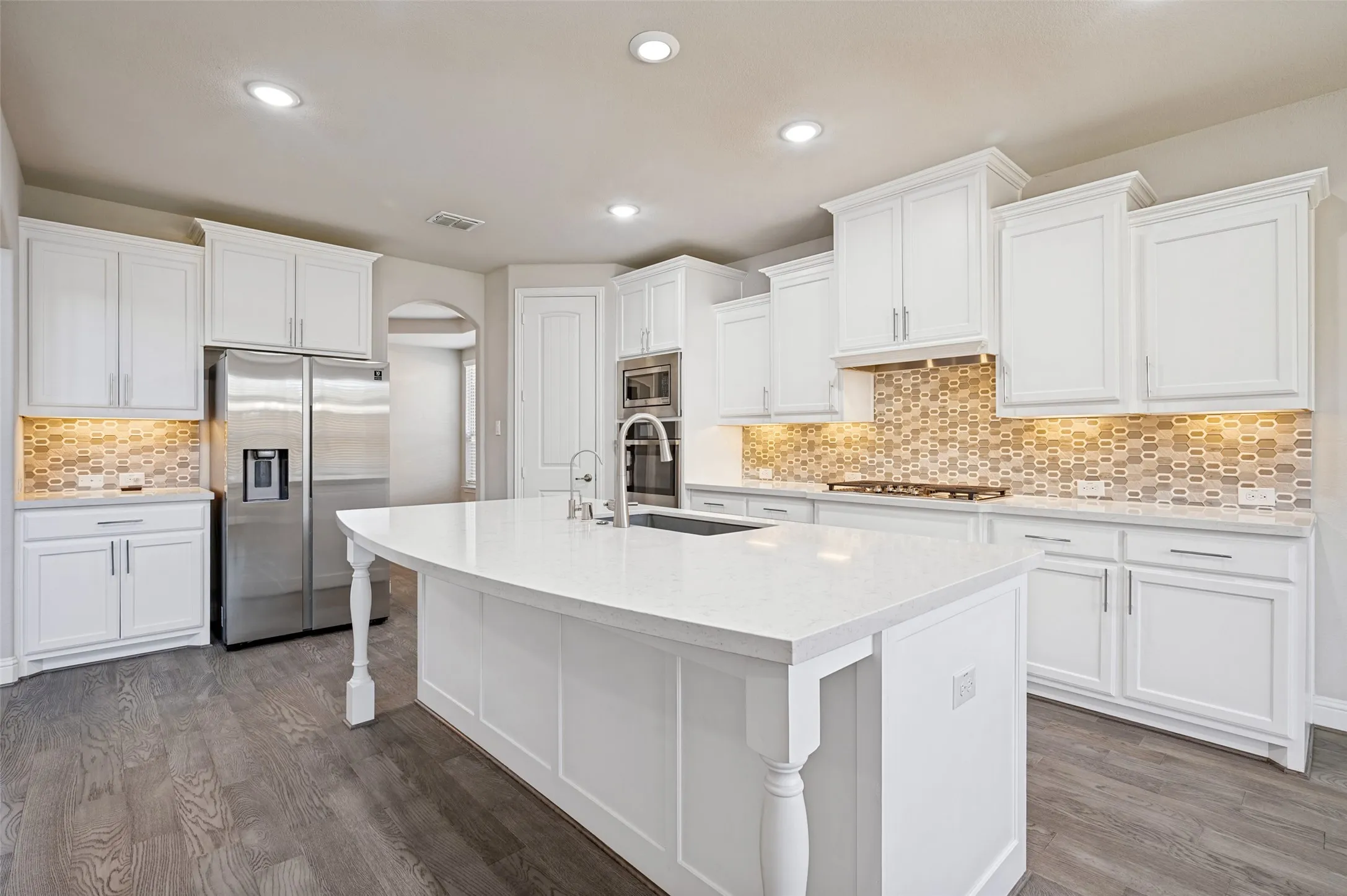 Kitchen featuring white cabinetry, stone countertops, stainless steel appliances, a tiled backsplash, and wood-finish flooring