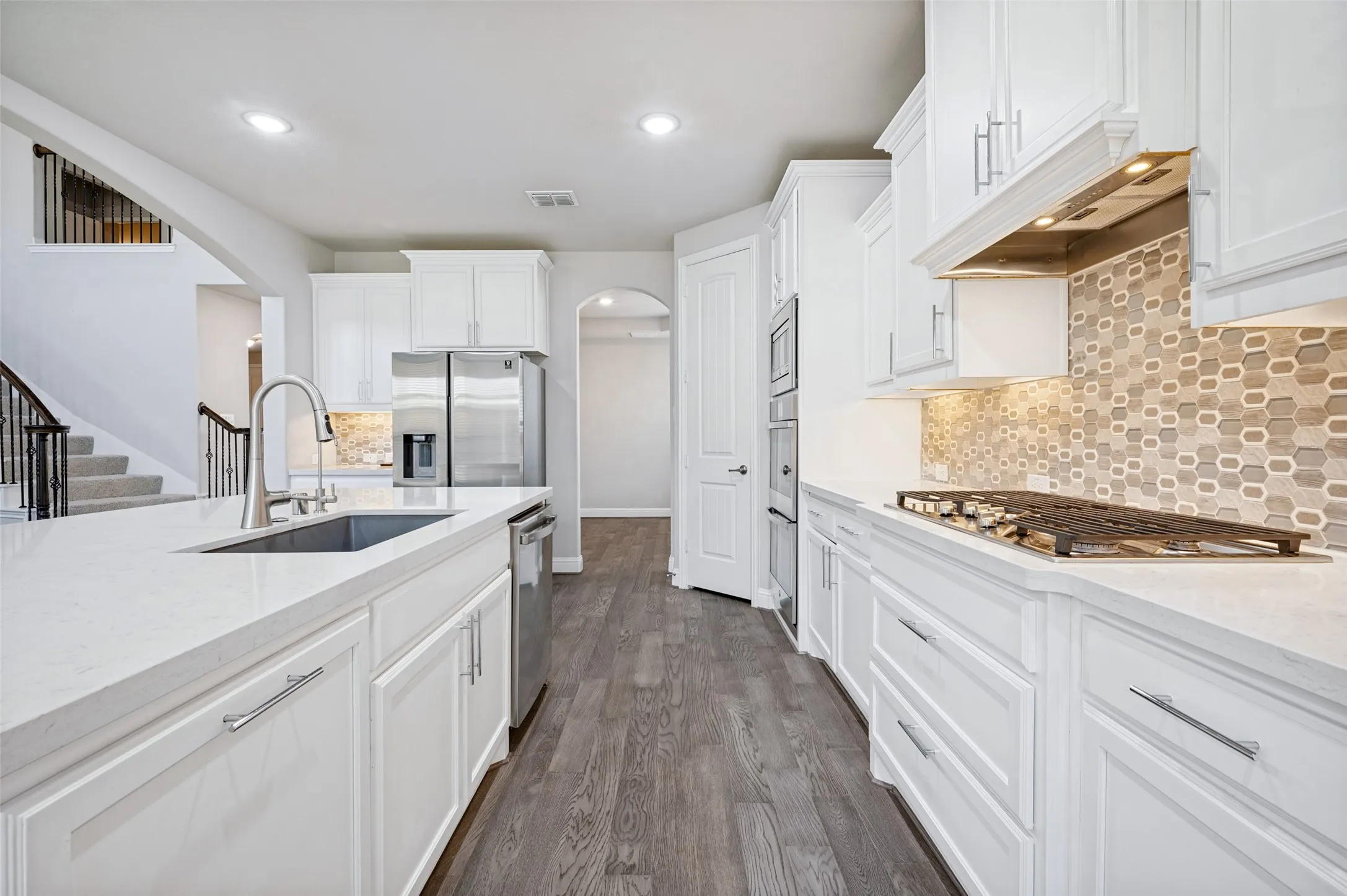 Gourmet kitchen featuring white cabinetry, light countertops, wood-finish flooring, a stainless steel refrigerator, and a mosaic tile backsplash