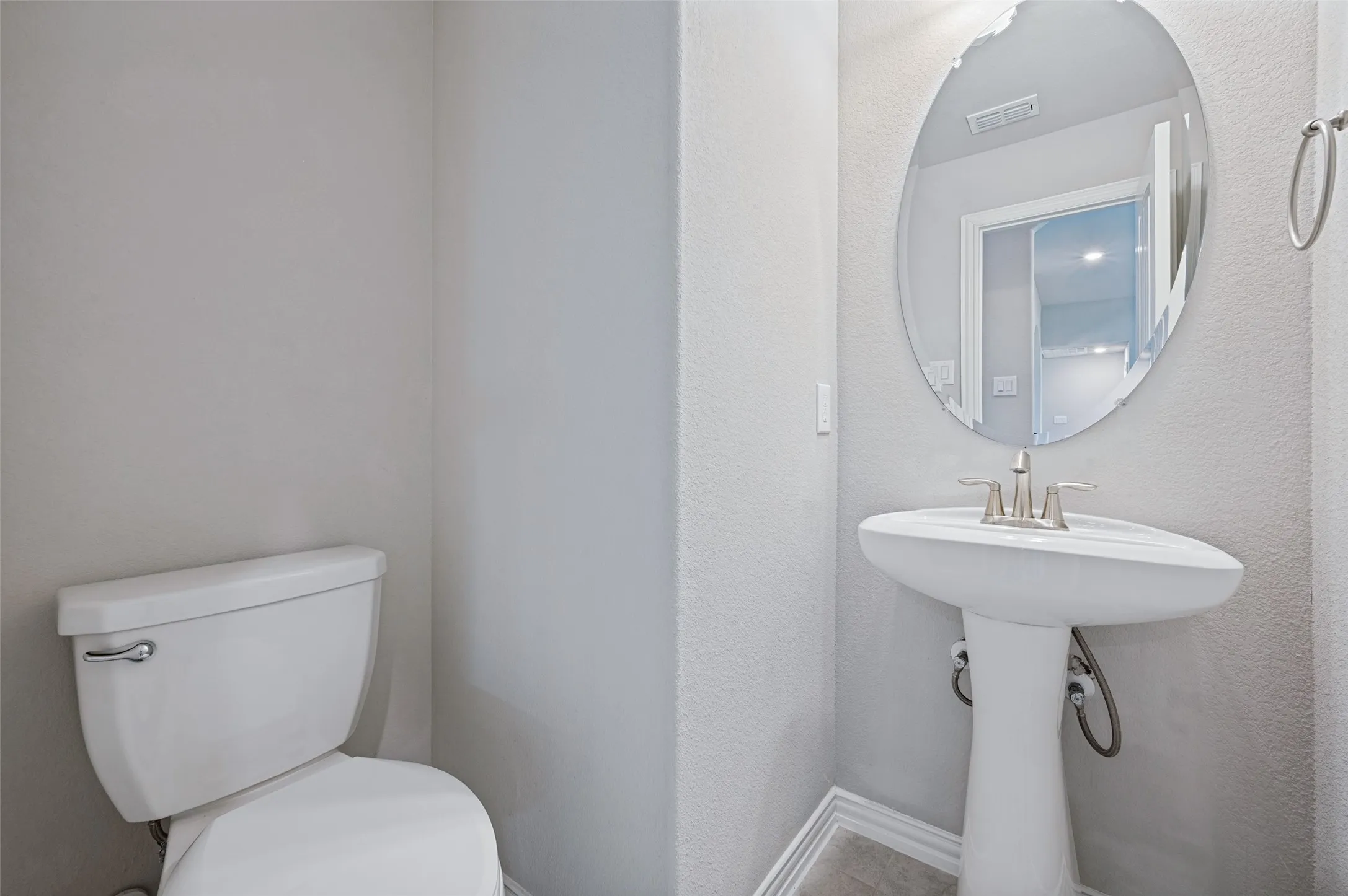 Pedestal sink with brushed nickel faucet, oval mirror, and tile flooring