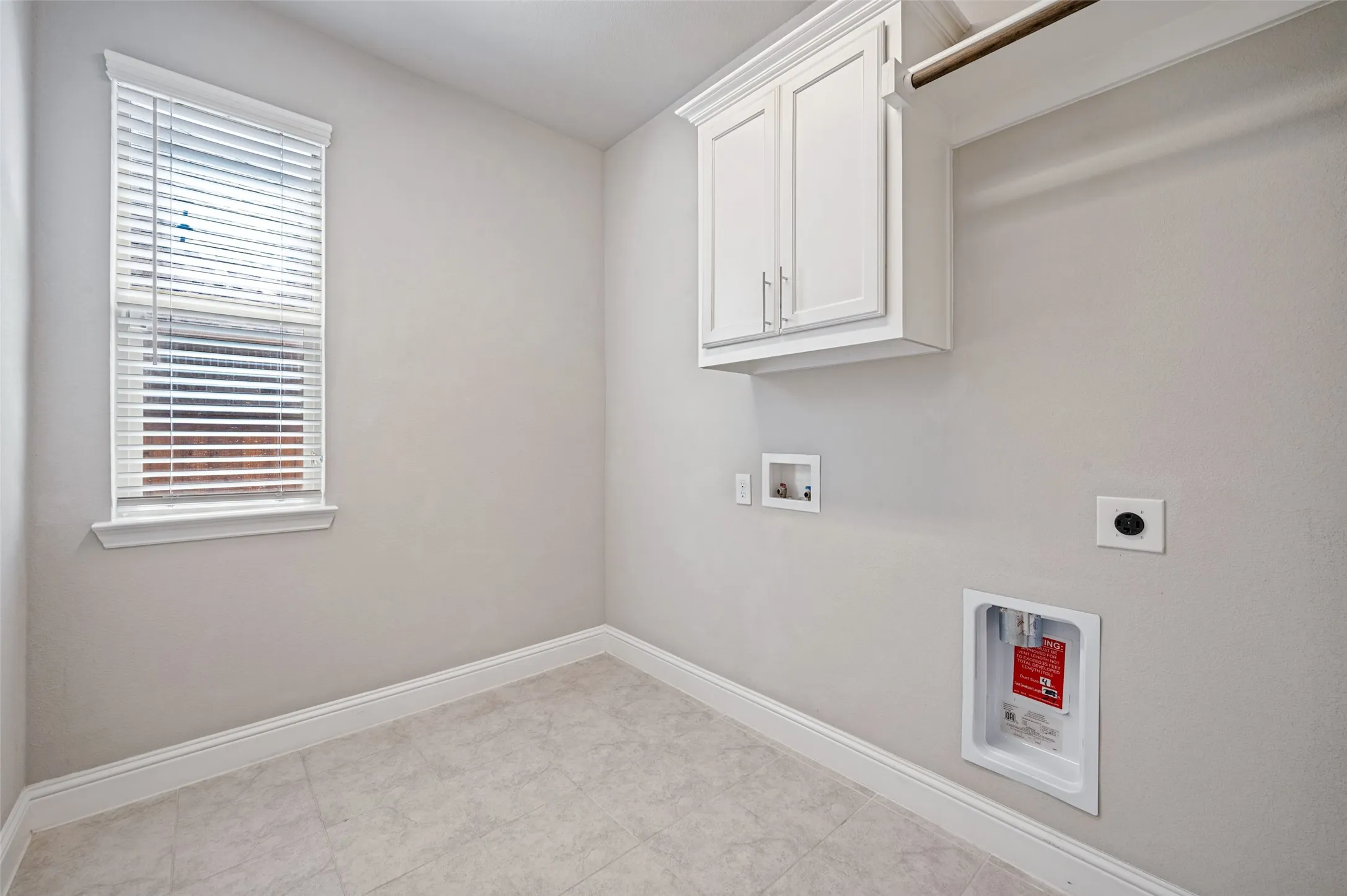 Laundry room featuring a window with blinds, upper cabinetry, a hanging rod, and tile flooring
