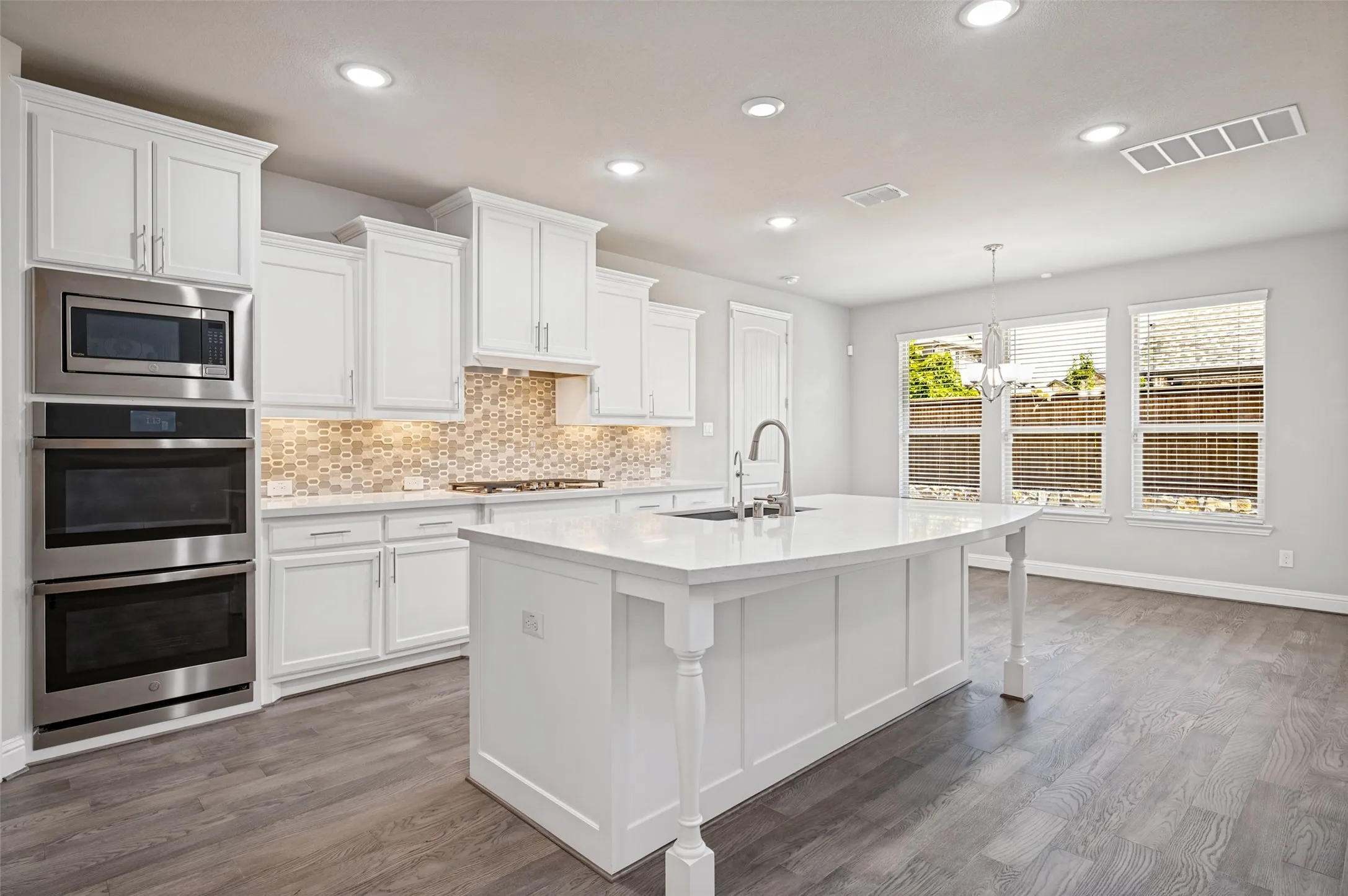 White cabinetry with stainless steel appliances, a large kitchen island with a basin sink, wood-finish flooring, and multiple windows