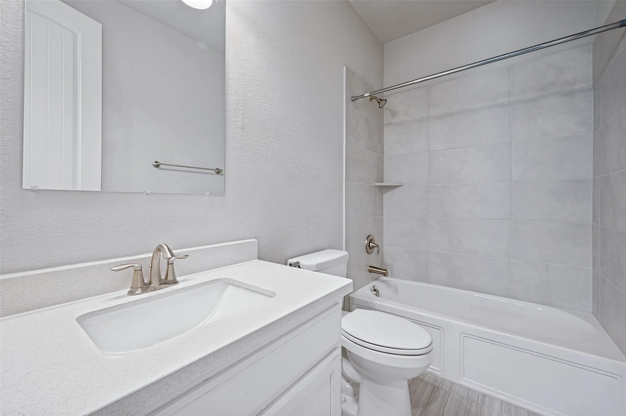 Bathroom featuring a vanity with an integrated sink, a rectangular mirror, a brushed nickel faucet, a white bathtub, and large format wall tiling