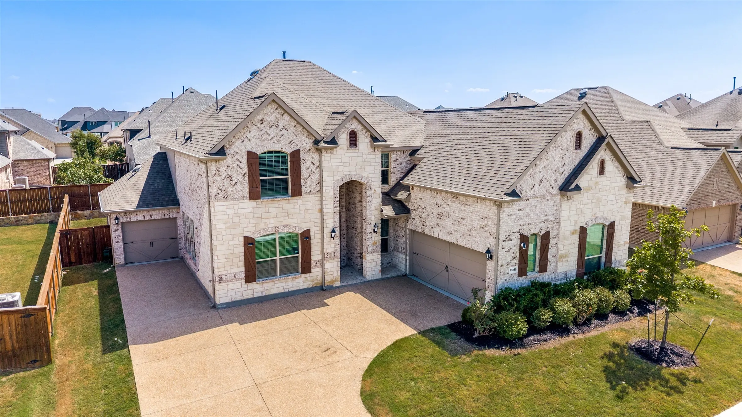 Stone facade with brick accents, multi-car garage, manicured landscaping, and a fenced backyard