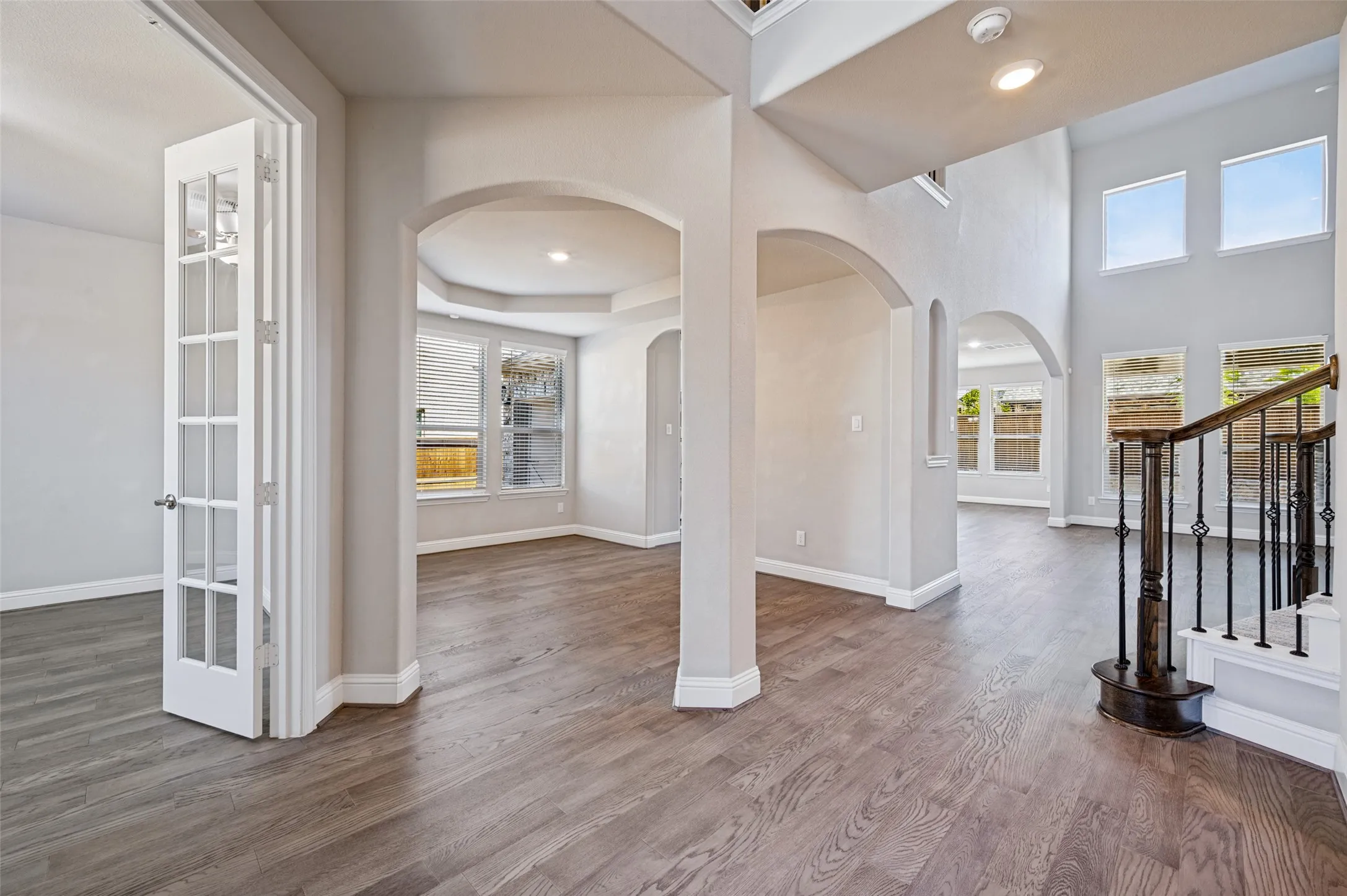 Wood-finish flooring throughout, arched doorways, French doors, a tray ceiling, and a prominent staircase with an ornate iron railing