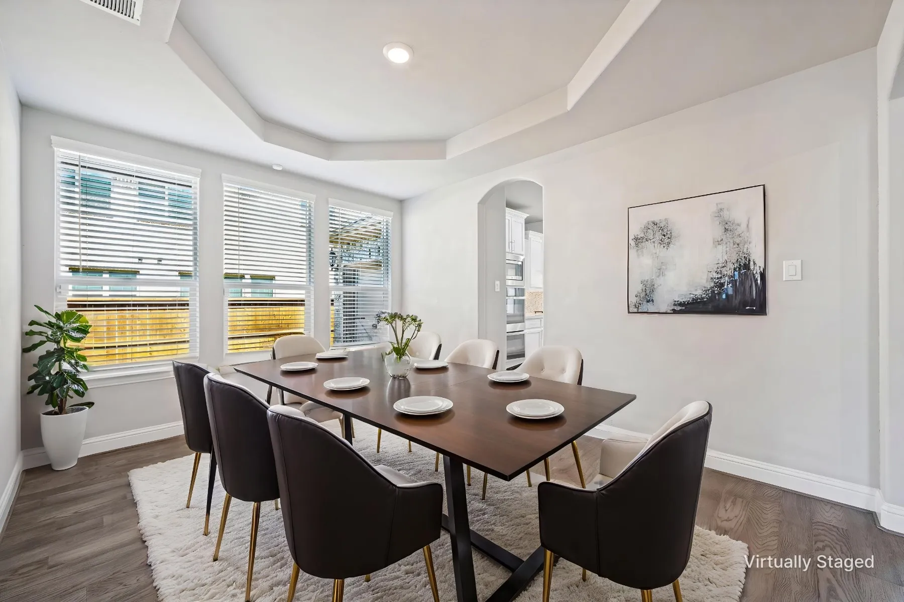 Tray ceiling with recessed lighting, multiple windows with blinds, wood-finish flooring, and an arched entryway