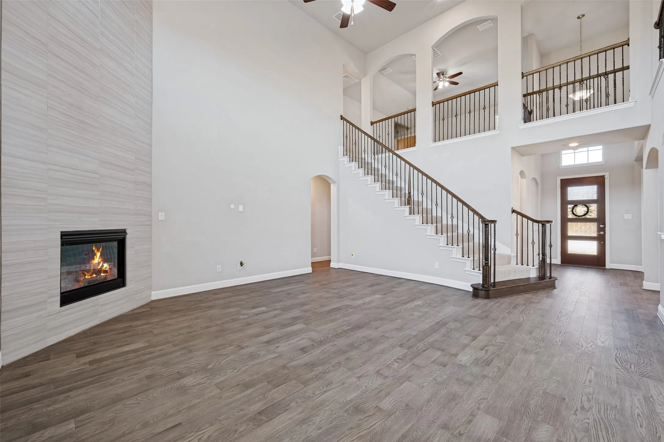 Vaulted ceiling, wood-finish flooring, fireplace with tile surround, wood staircase with metal balusters, and a solid wood entry door with frosted glass panels