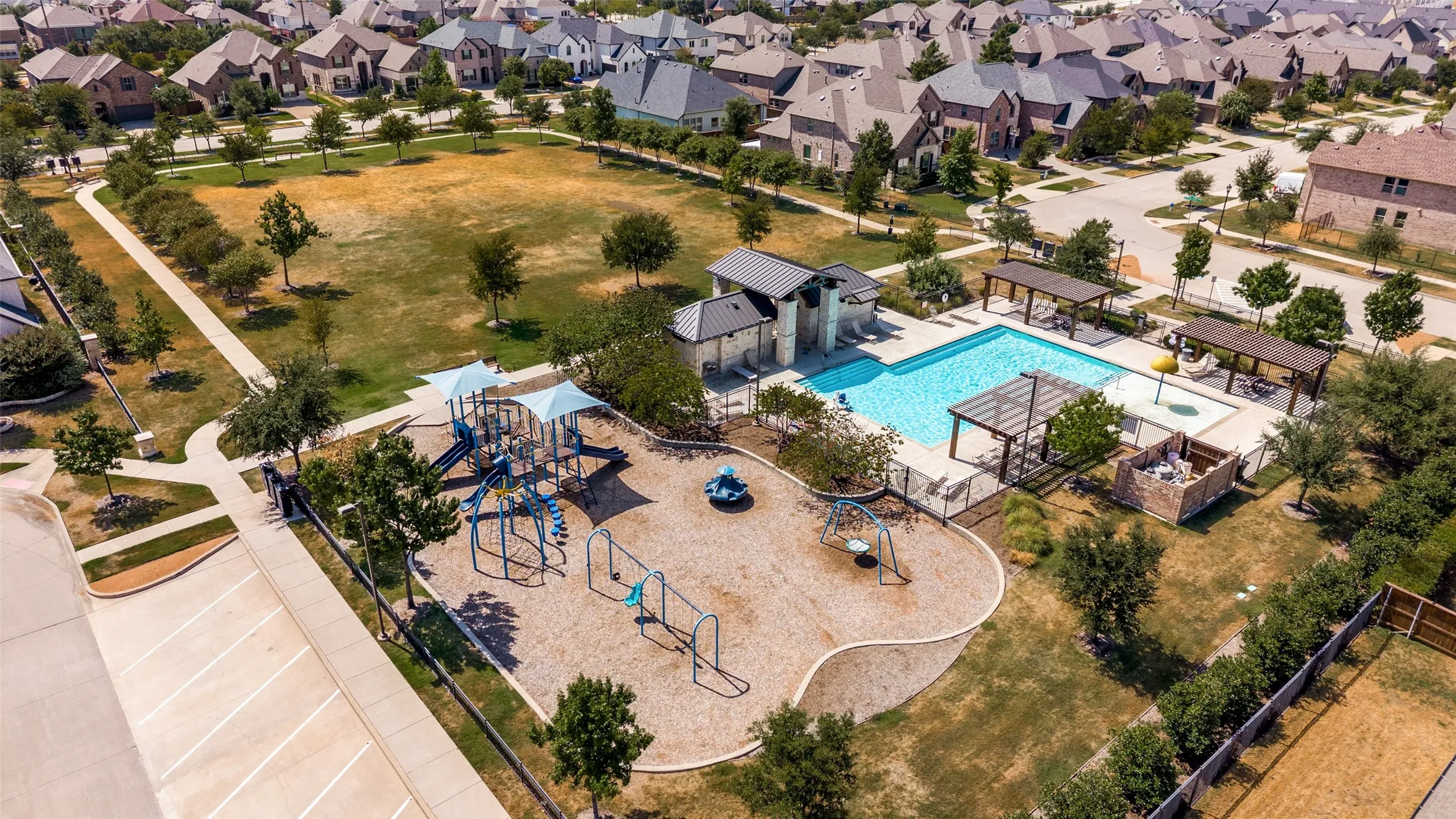 Community pool with shaded pergolas, adjacent playground, and expansive open green space