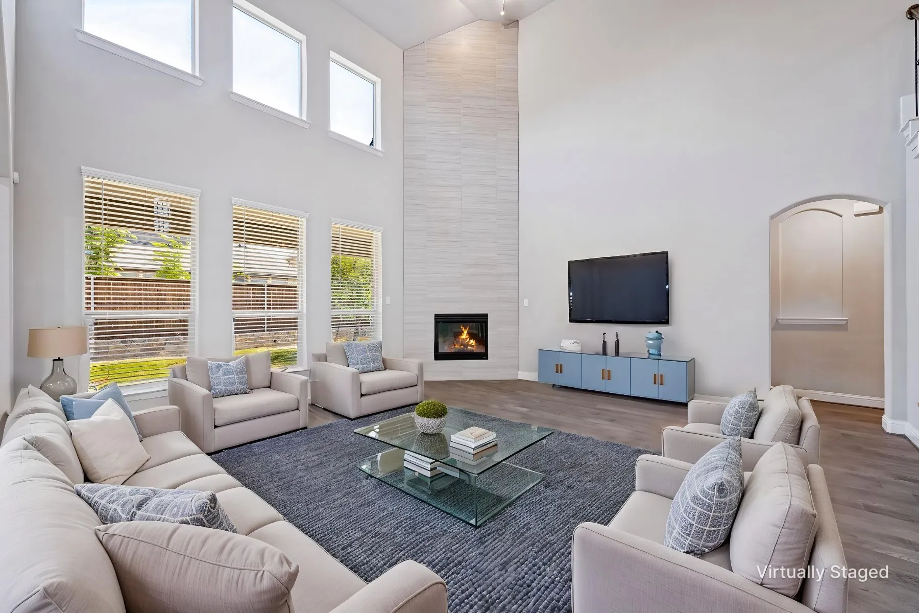 Two-story living area with high ceilings, multiple windows, a gas fireplace with a tiled surround, and wood-finish flooring