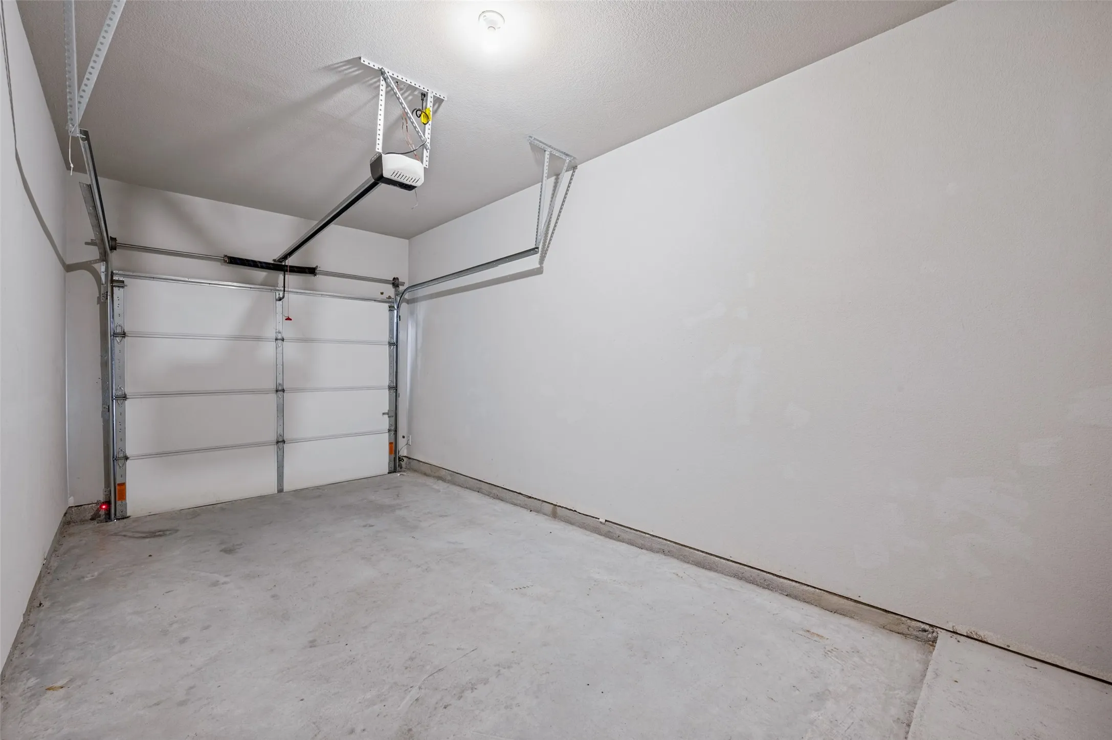 Single-car garage with a concrete floor, white walls, and an overhead garage door opener