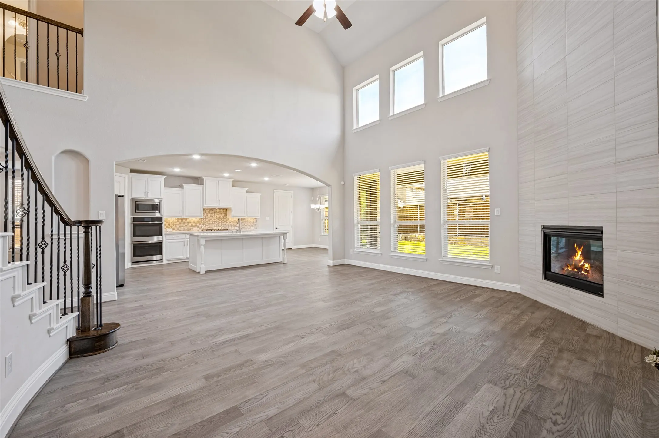 Soaring vaulted ceilings, wood-finish flooring, a modern fireplace with a tiled surround, and multiple windows