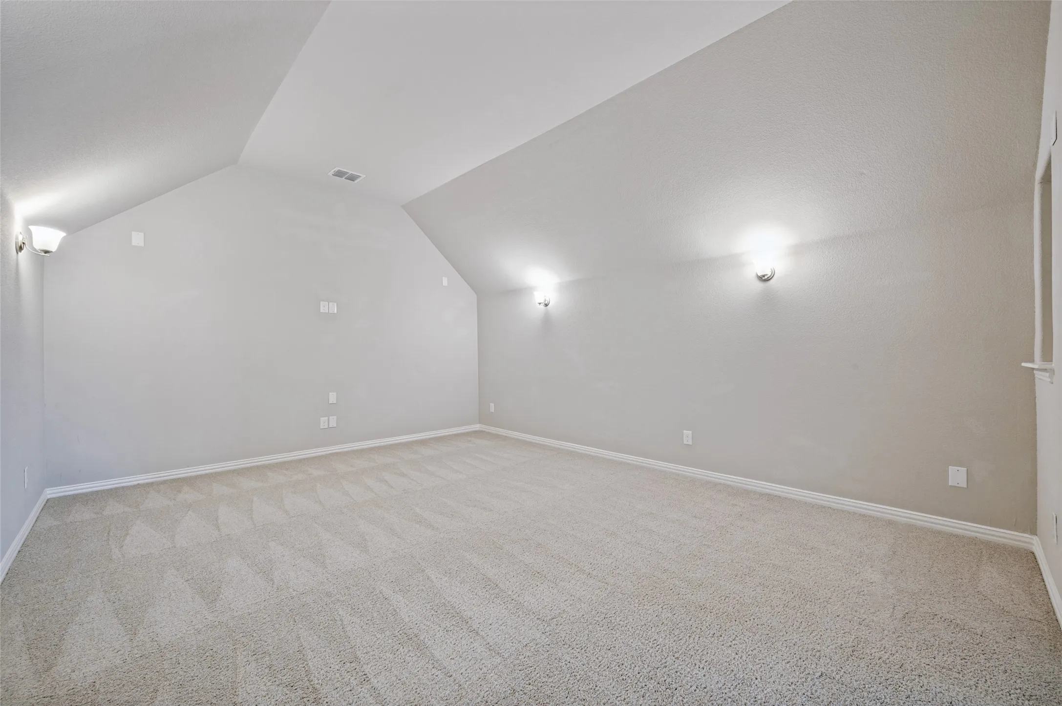 Media room featuring sloped ceilings, wall-mounted sconce lighting, and neutral carpeting