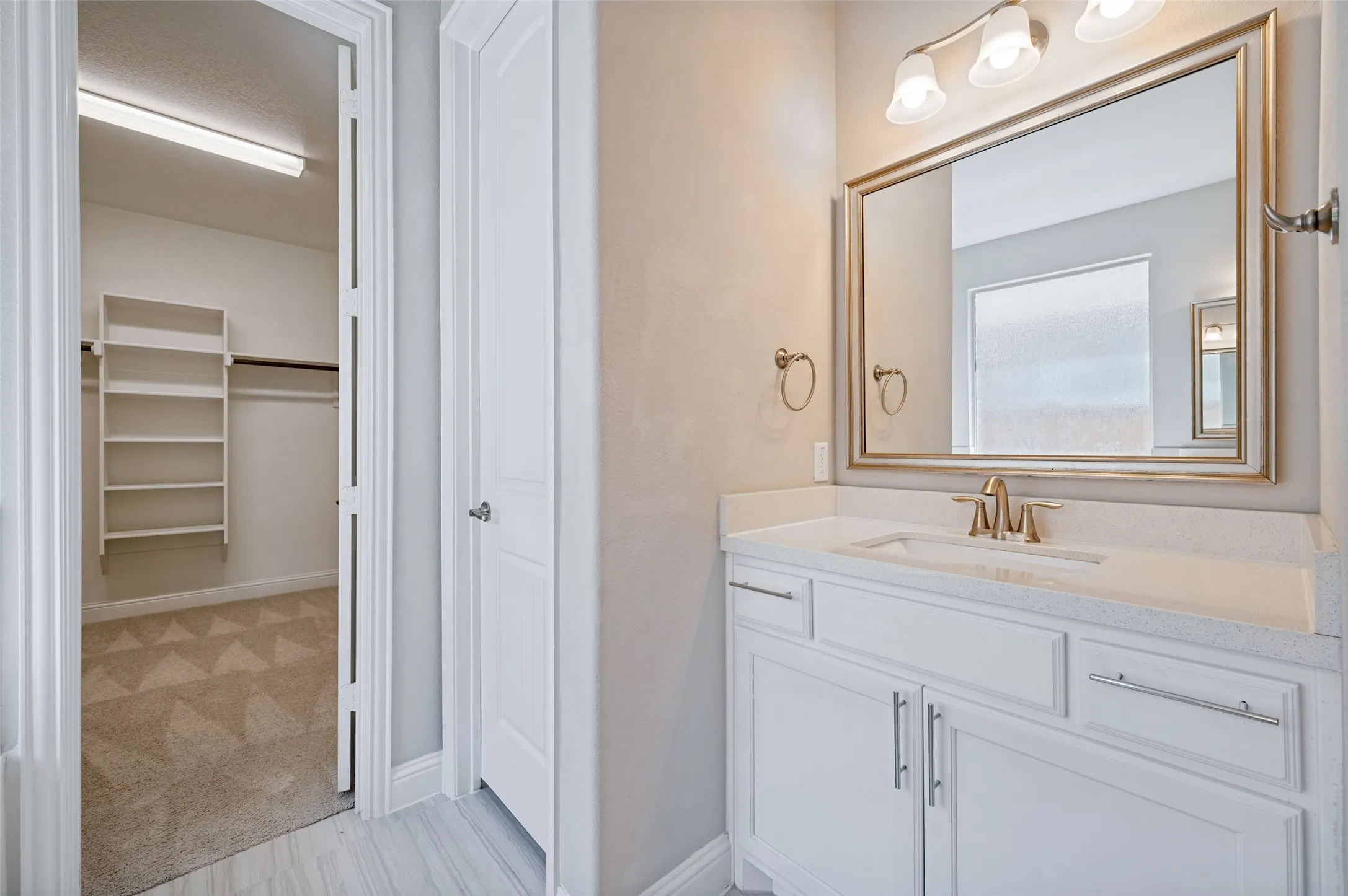 White vanity with integrated sink, gold-framed mirror, and a three-light fixture