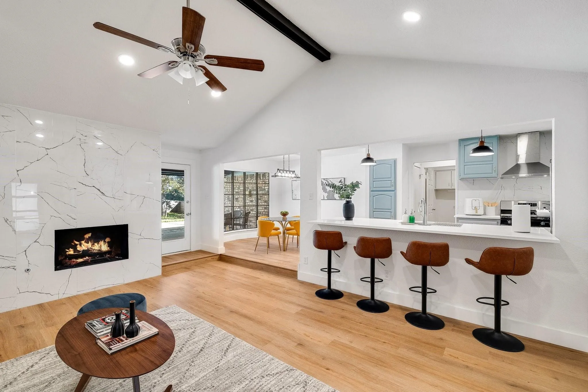 Vaulted ceilings, wood-finish flooring, a contemporary fireplace with a stone surround, and an open breakfast bar with pendant lighting