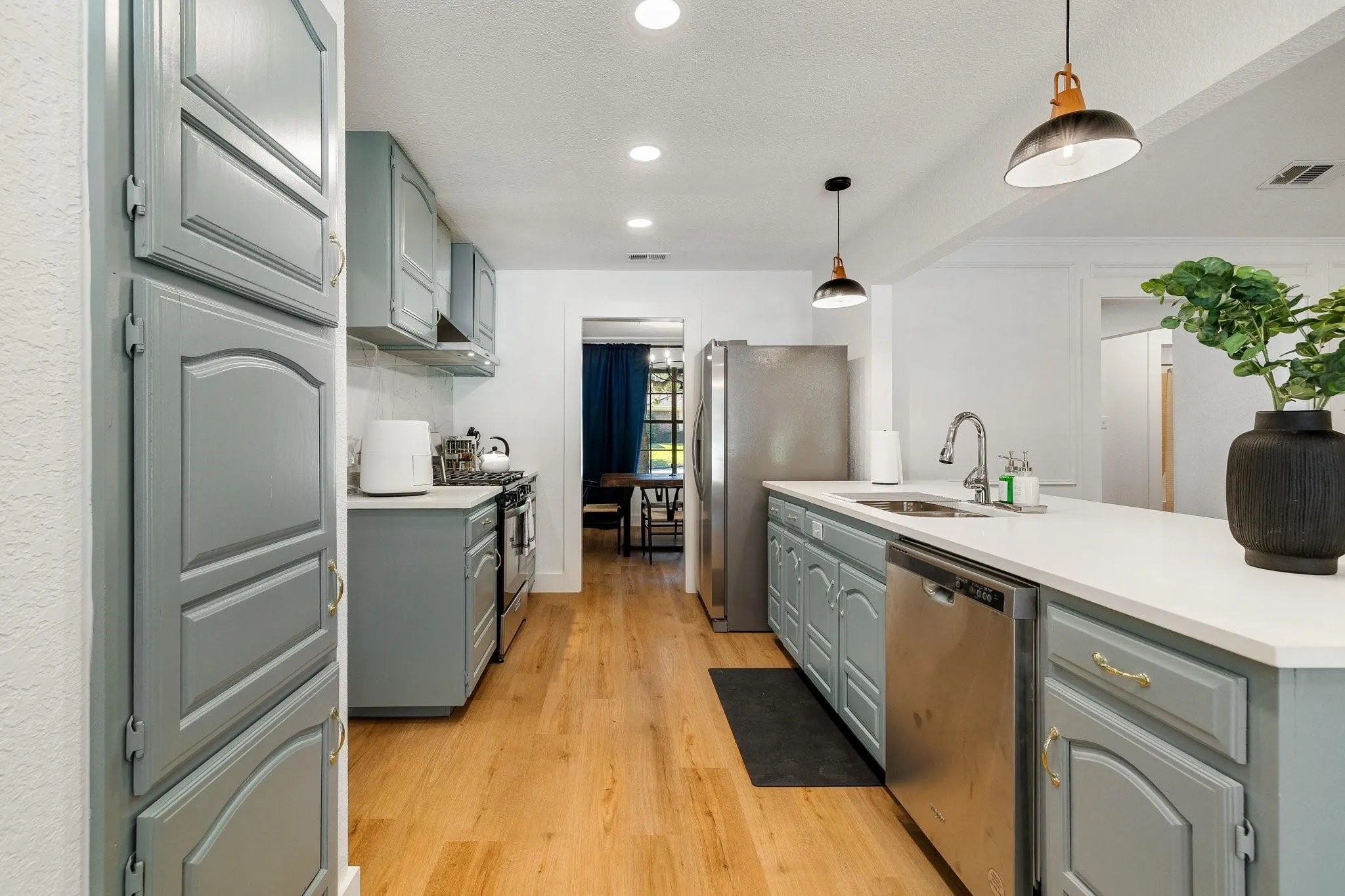 Kitchen featuring light-toned wood-finish flooring, light blue cabinetry with gold-tone hardware, stainless steel appliances, white countertops, and recessed lighting