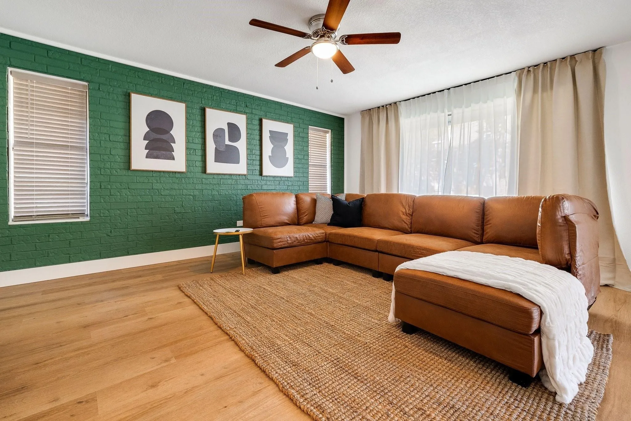 Light wood-finish flooring, accent brick wall, recessed lighting, ceiling fan, and large windows with privacy blinds