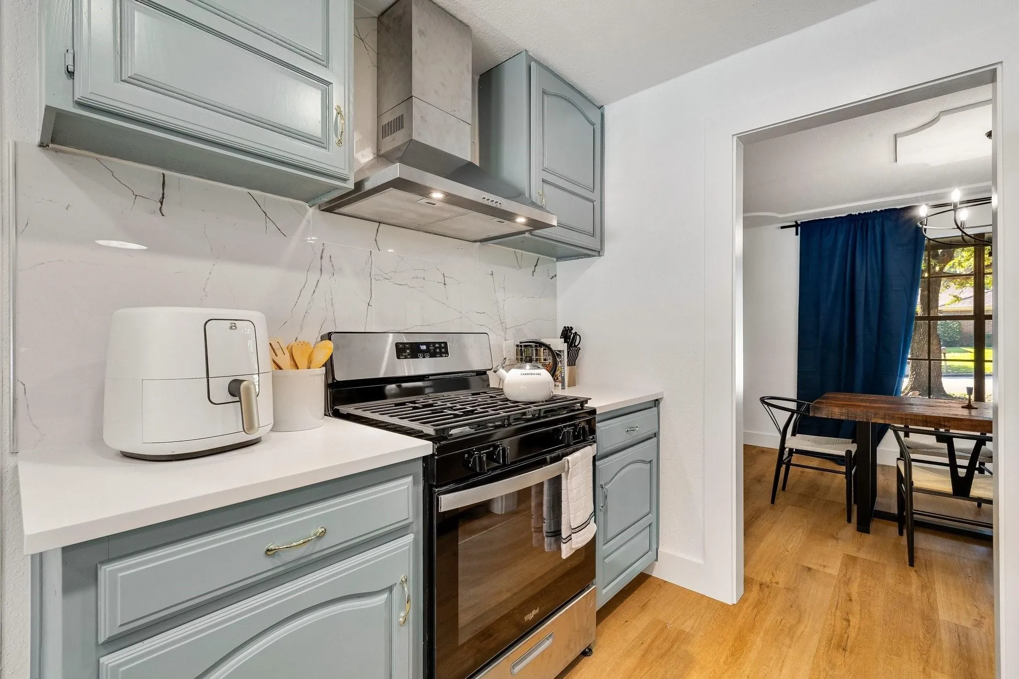 Light blue cabinetry with gold-tone hardware, white countertops, and a white backsplash featuring grey veining